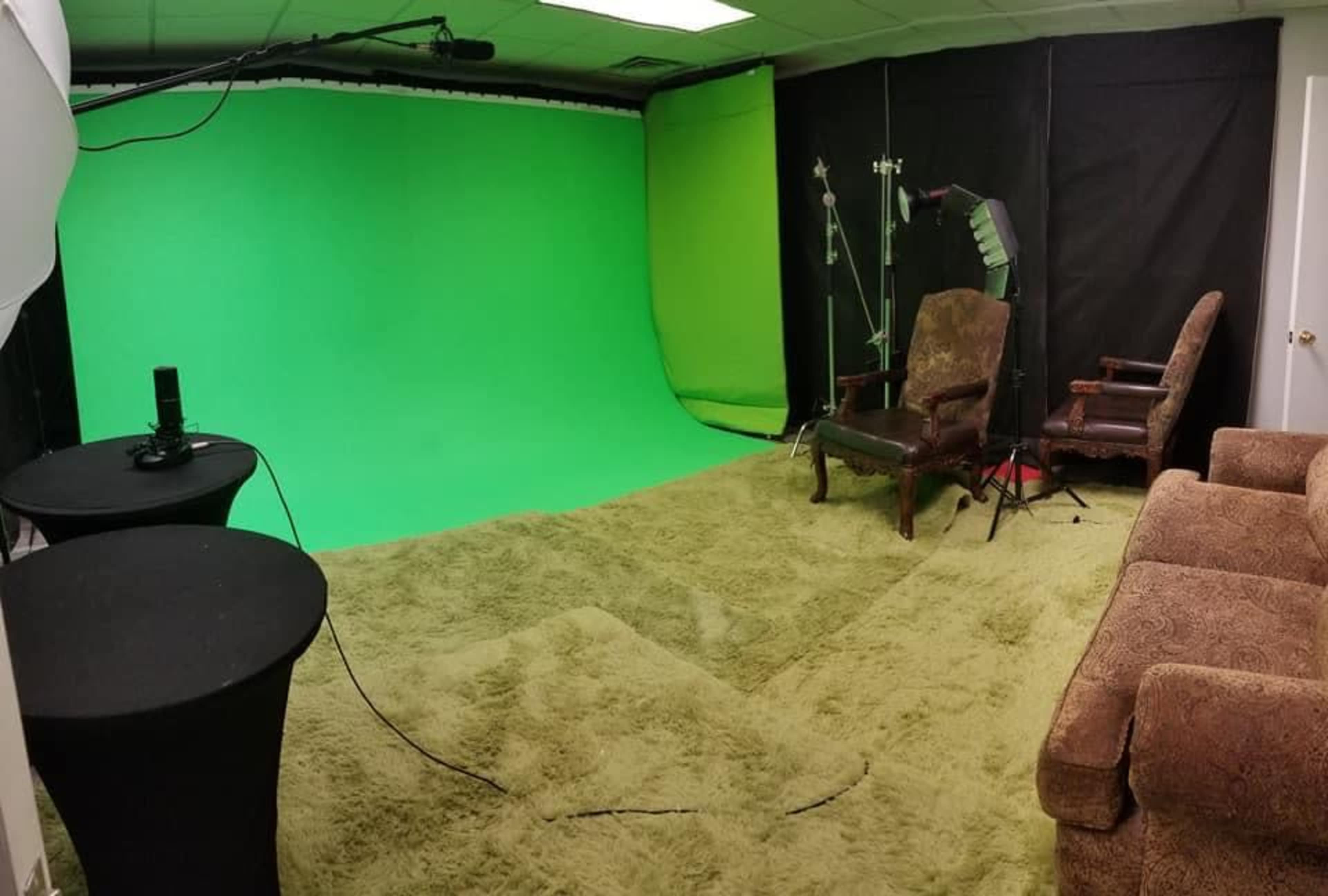 A room with a green backdrop, two chairs, and equipment for lighting and recording.