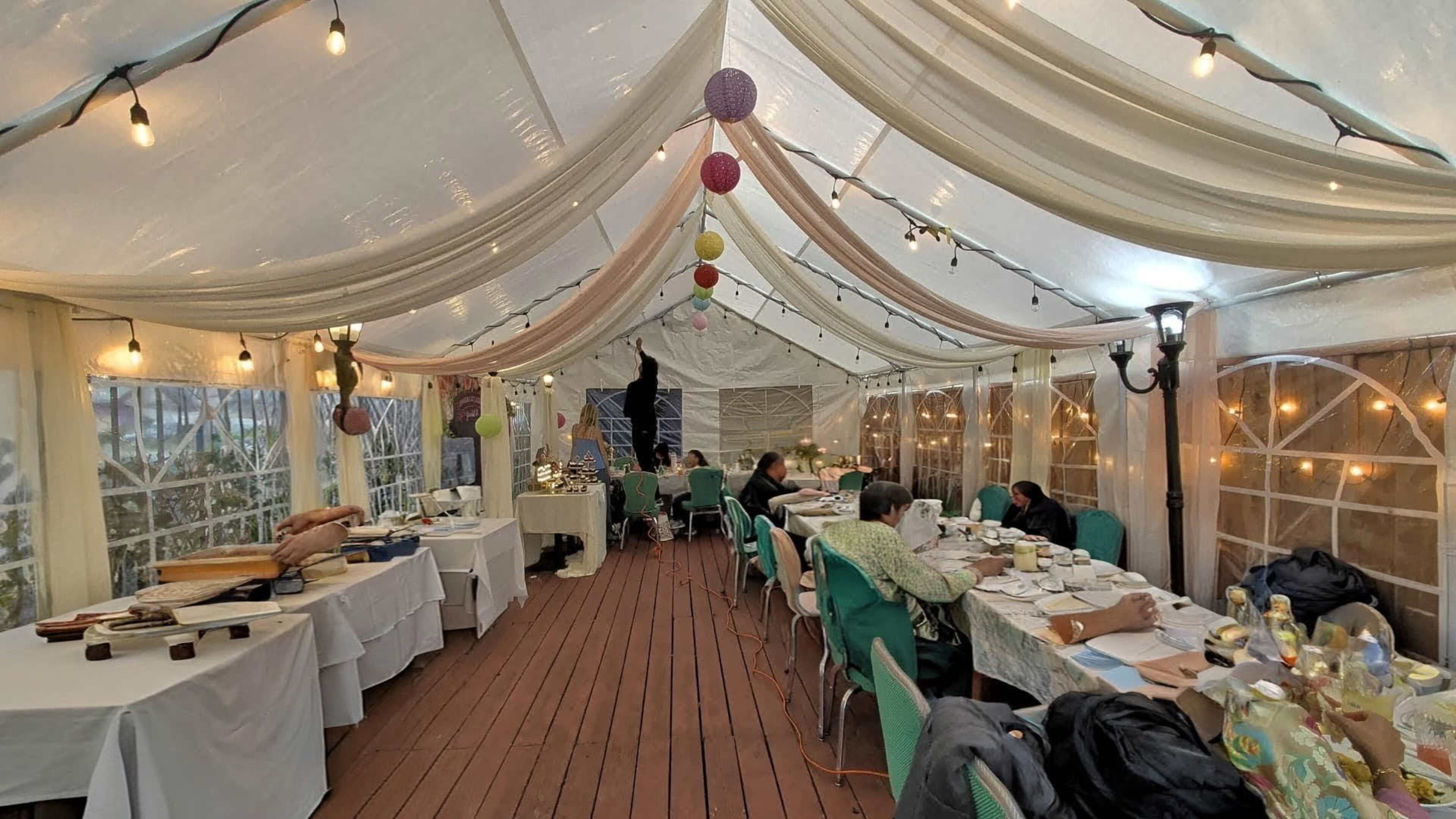 The image shows a decorated tent with tables set for a dining event, including various food displays and guests seated at tables.