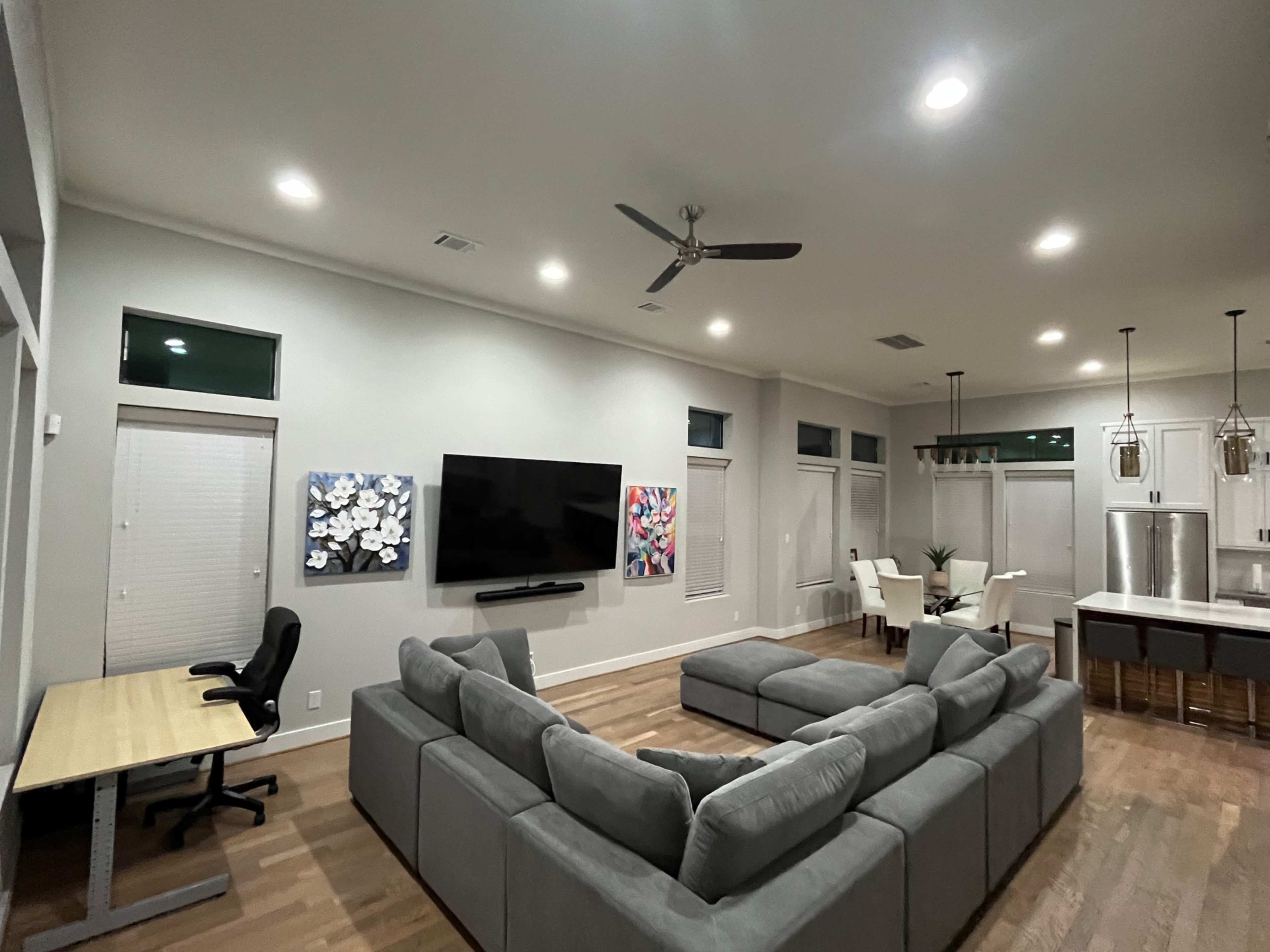 A modern living room with a sectional sofa, a wall-mounted television, and a dining area in the background.