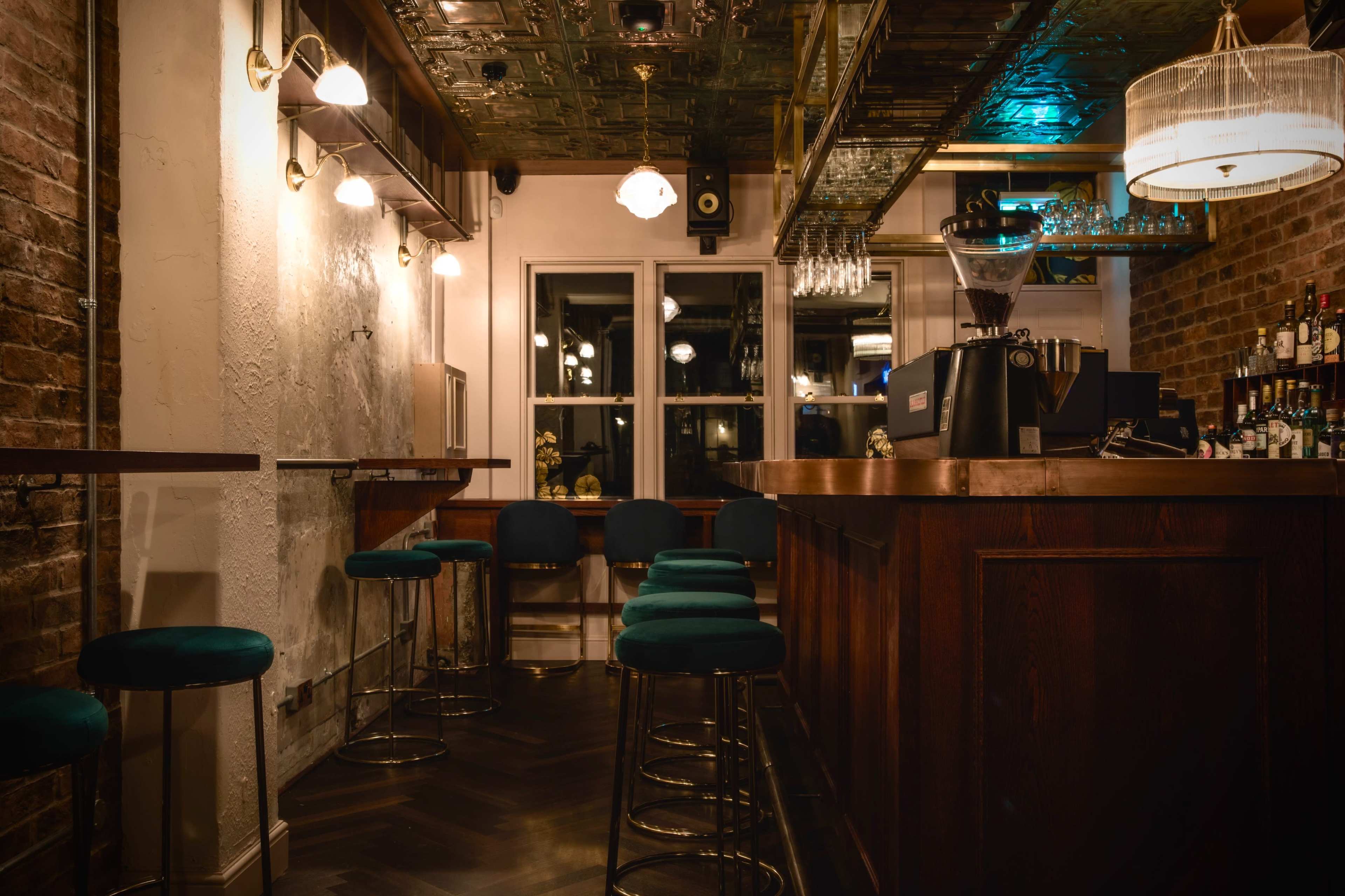 A dimly lit bar with wooden furnishings, green bar stools, and shelves filled with bottles in a stylish interior.