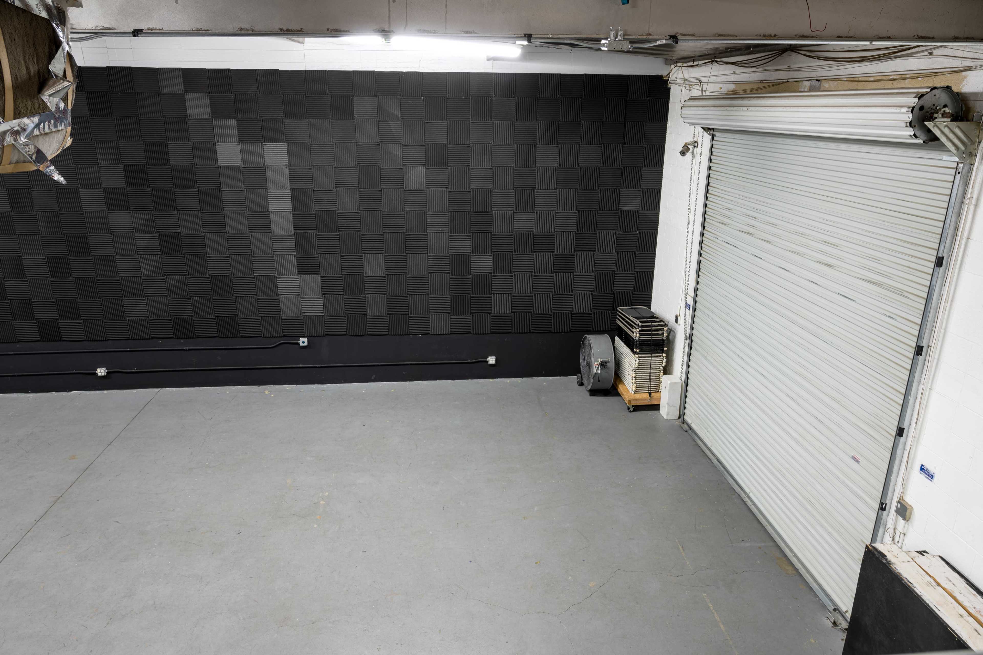 A spacious, empty room with a textured black wall and a closed roll-up door on one side.