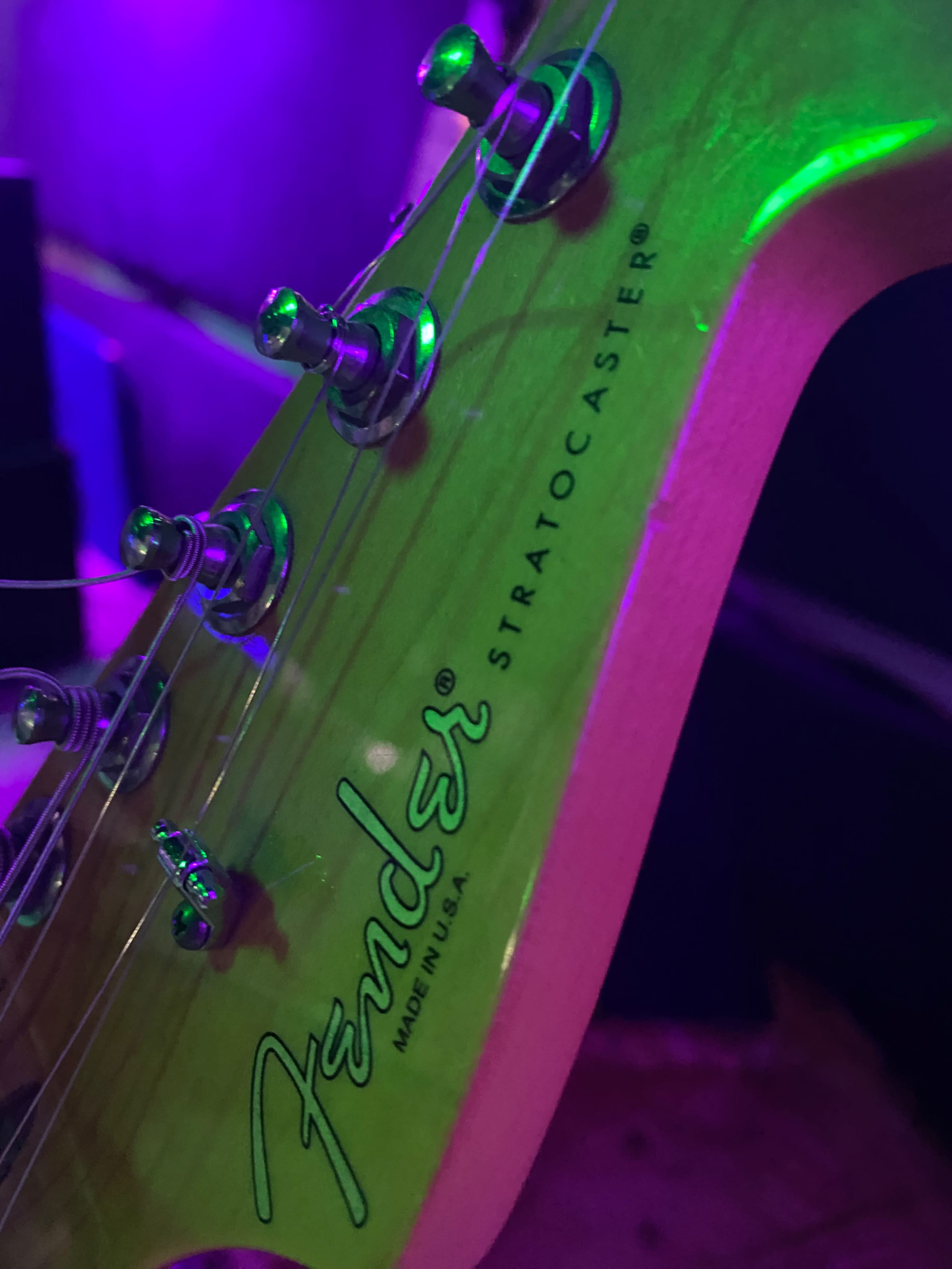 The image shows the headstock of a Fender Stratocaster guitar with tuning pegs and the Fender logo visible.
