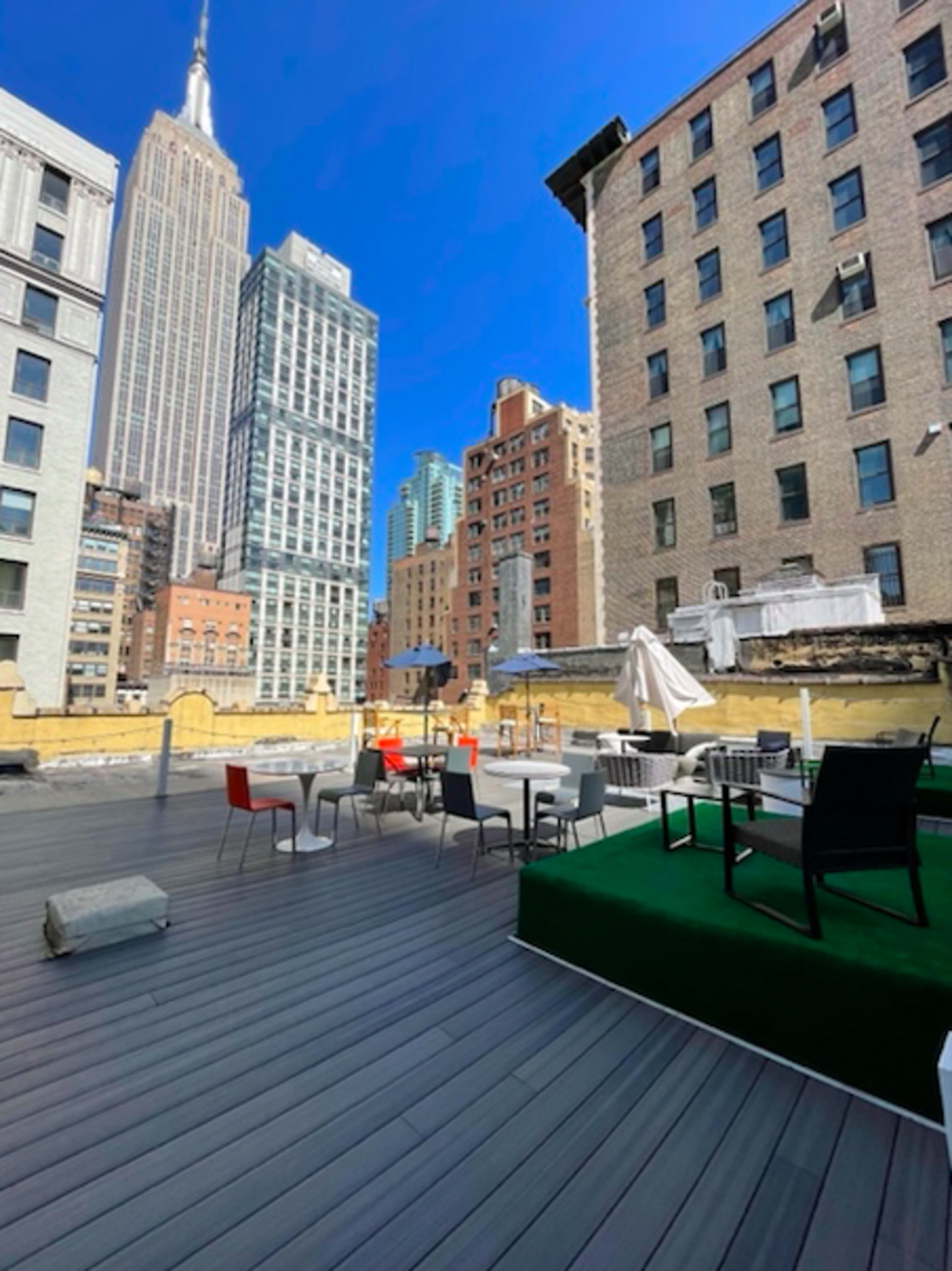 A rooftop patio features modern seating and greenery with the Empire State Building visible in the background.