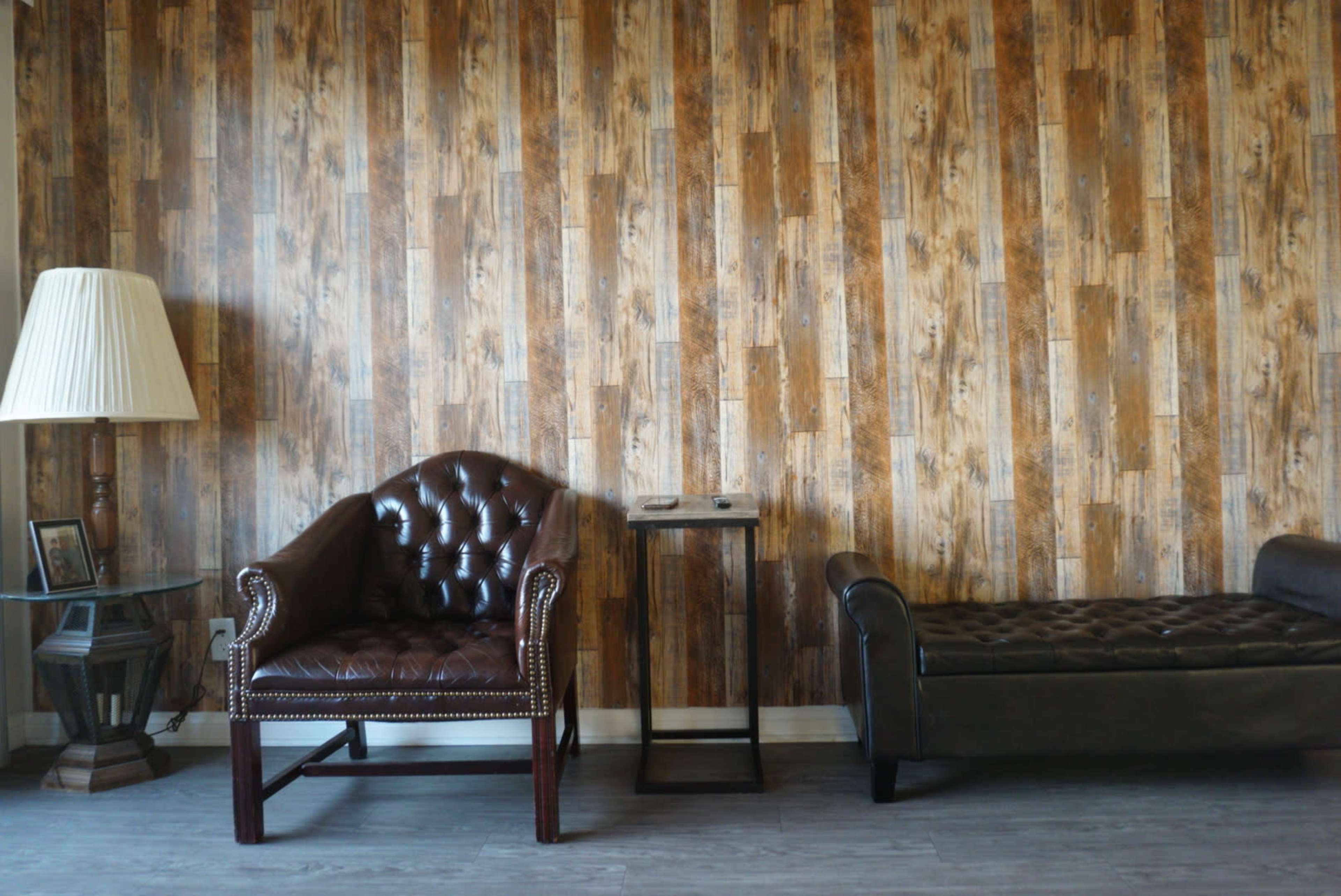A room with a patterned wooden wall, a brown leather armchair, a small side table, a lamp, and a black sofa.