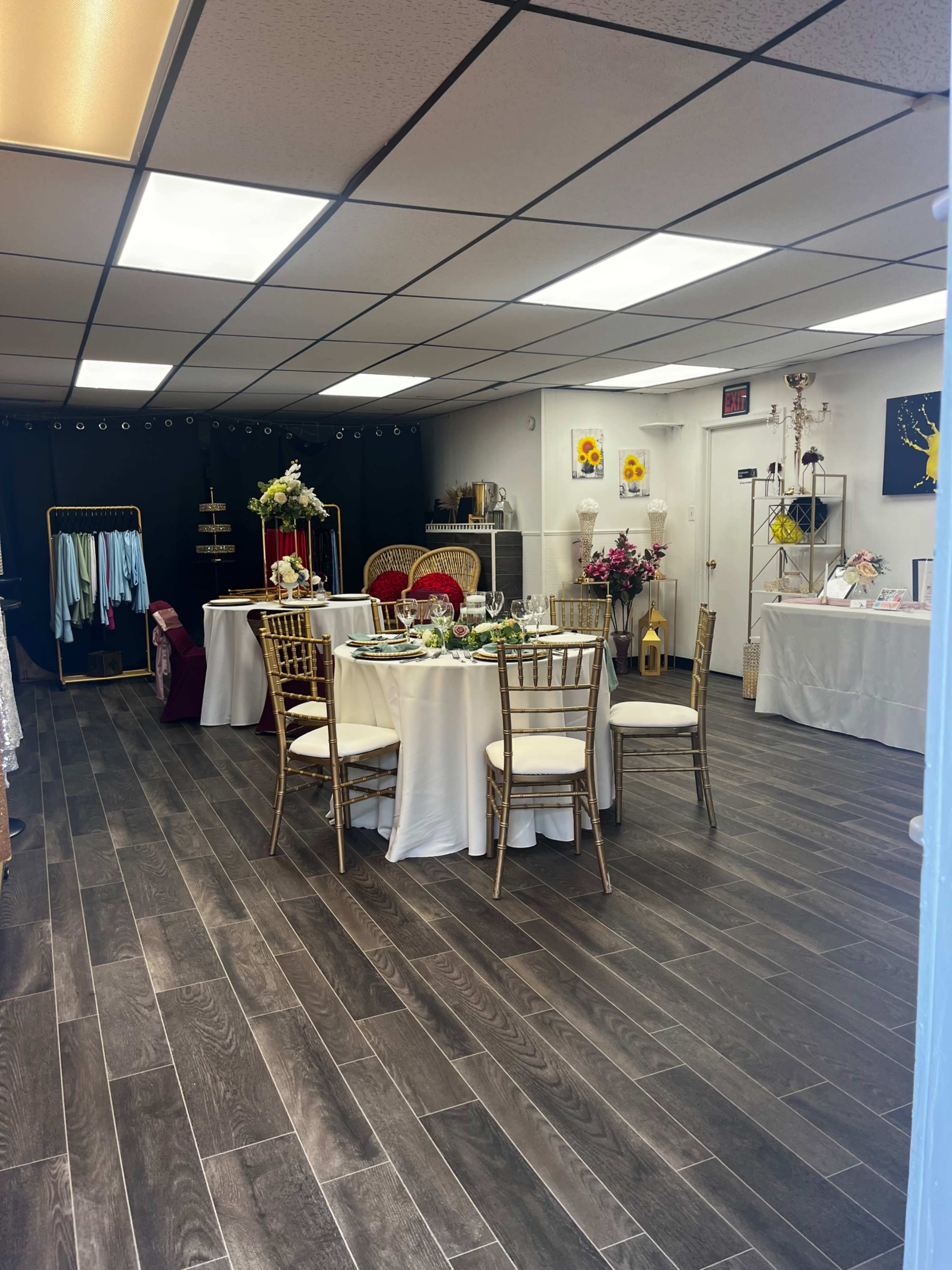 The image shows a neatly arranged event space with tables set for dining, surrounded by clothing displays and decorative elements.