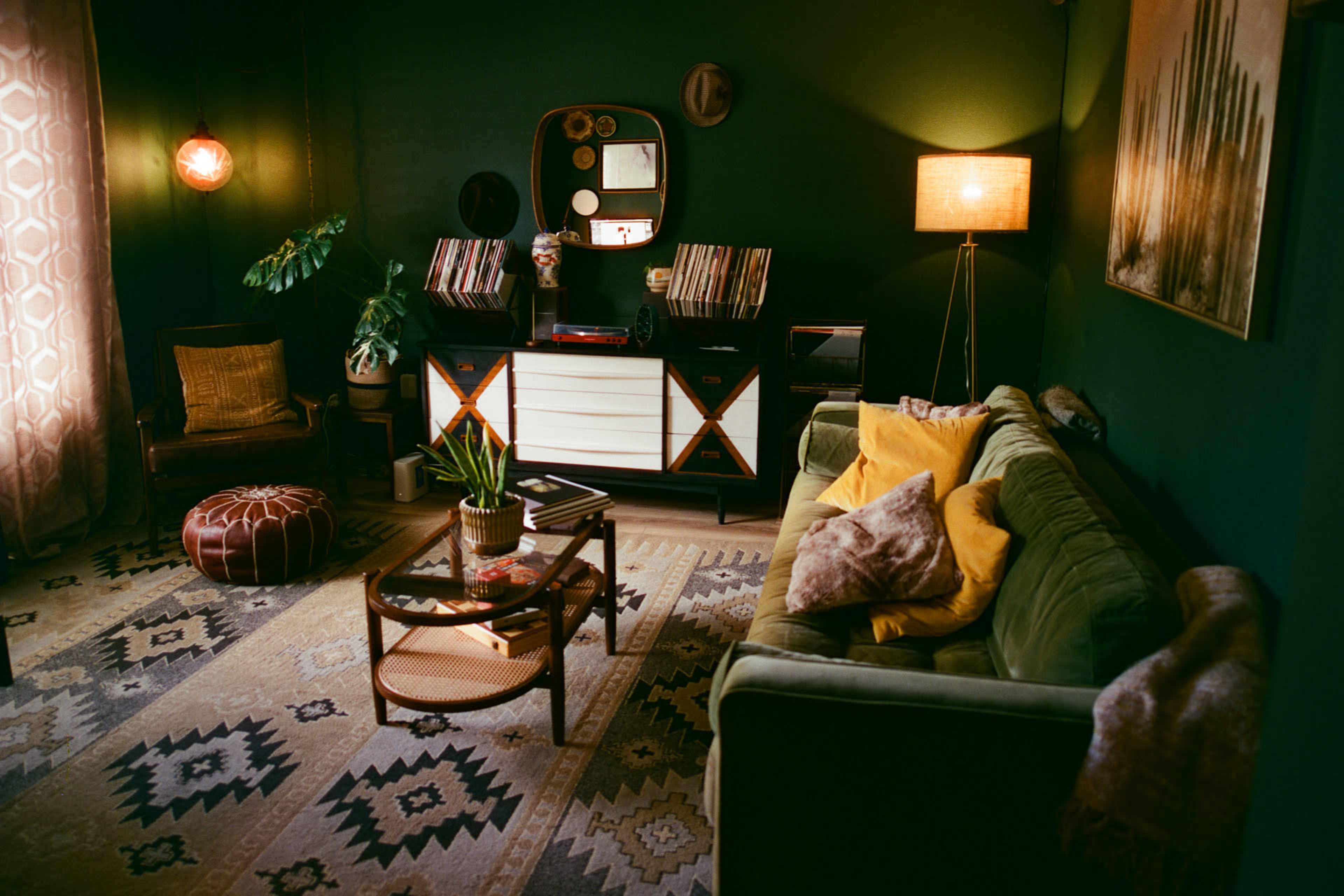 The image shows a cozy living room with a green wall, a sofa, a record player, and decorative elements like plants and a patterned rug.