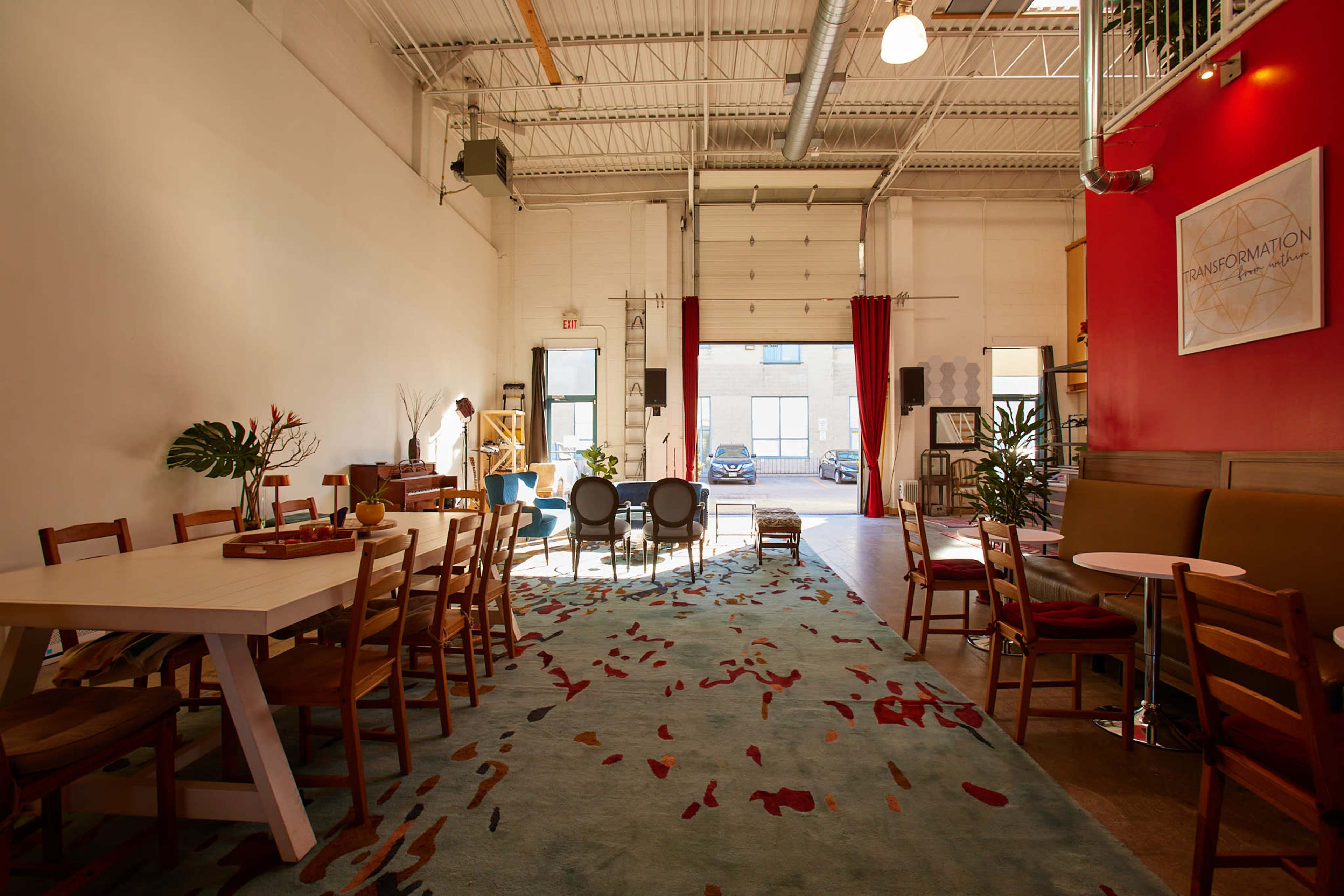 A spacious interior with a dining area featuring a large table, chairs, and a colorful area rug, leading to an open entry with large doors.