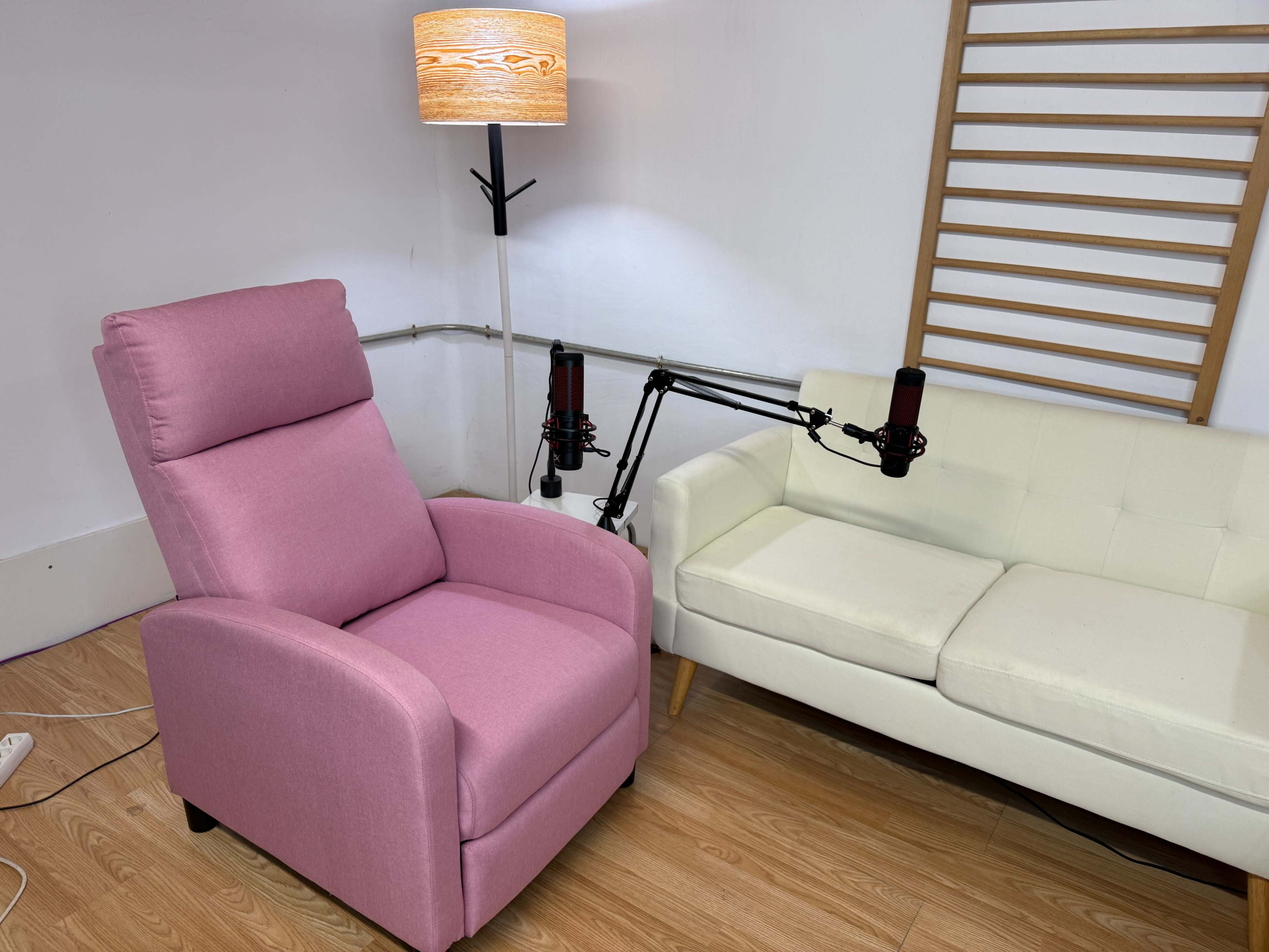The image shows a pink reclining chair next to a white sofa, both placed in a room with a wooden floor and a lamp.