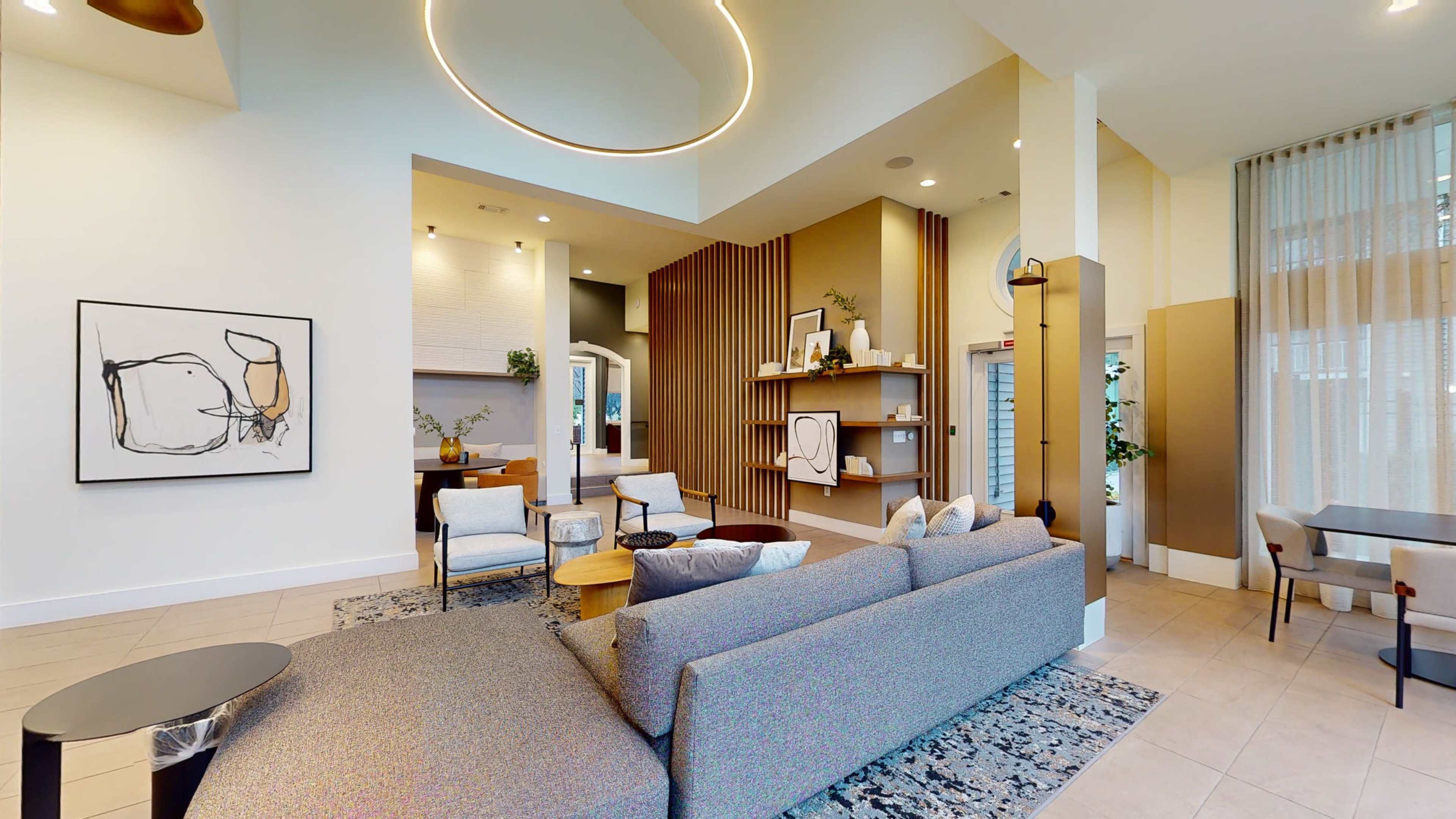 A modern indoor lounge area featuring a gray sectional sofa, minimalist artwork on the walls, and various decorative shelves and plants.
