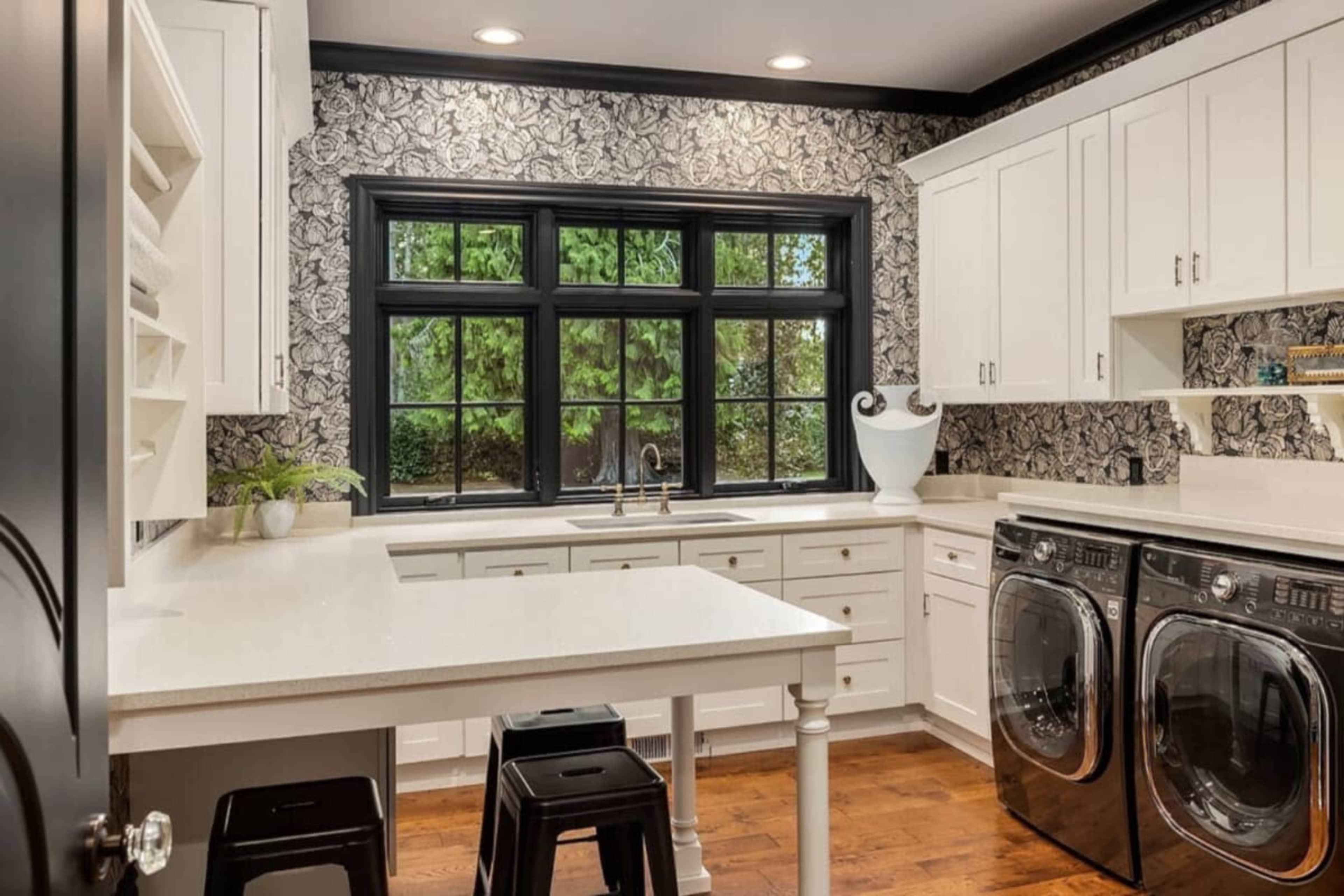 The image shows a modern kitchen with a laundry area featuring white cabinetry, dark accents, and a large window with black trim.