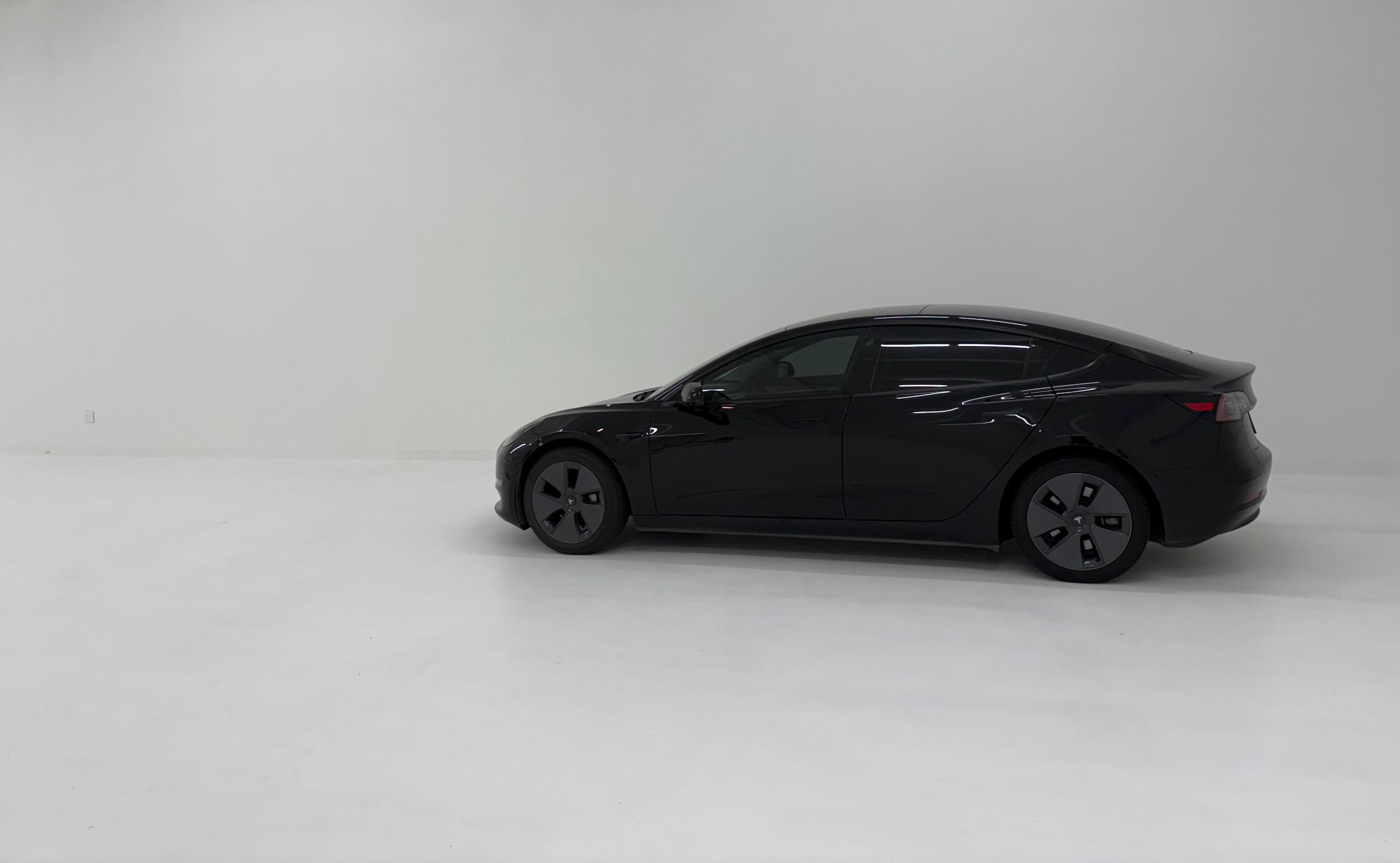 A black sedan is parked in a spacious, minimalistic white room.
