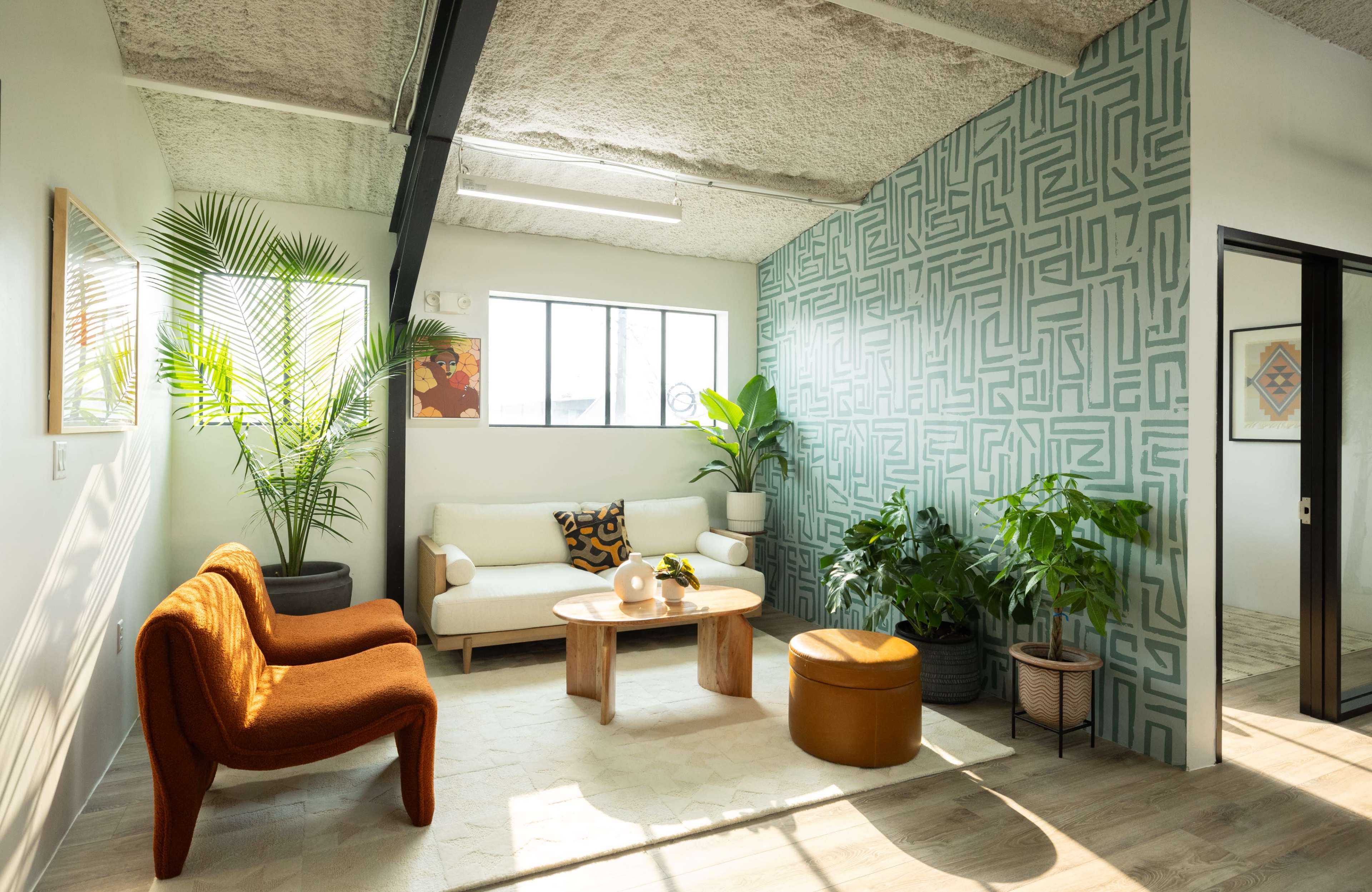A modern living room with a patterned accent wall, a beige sofa, a wooden coffee table, and various indoor plants.