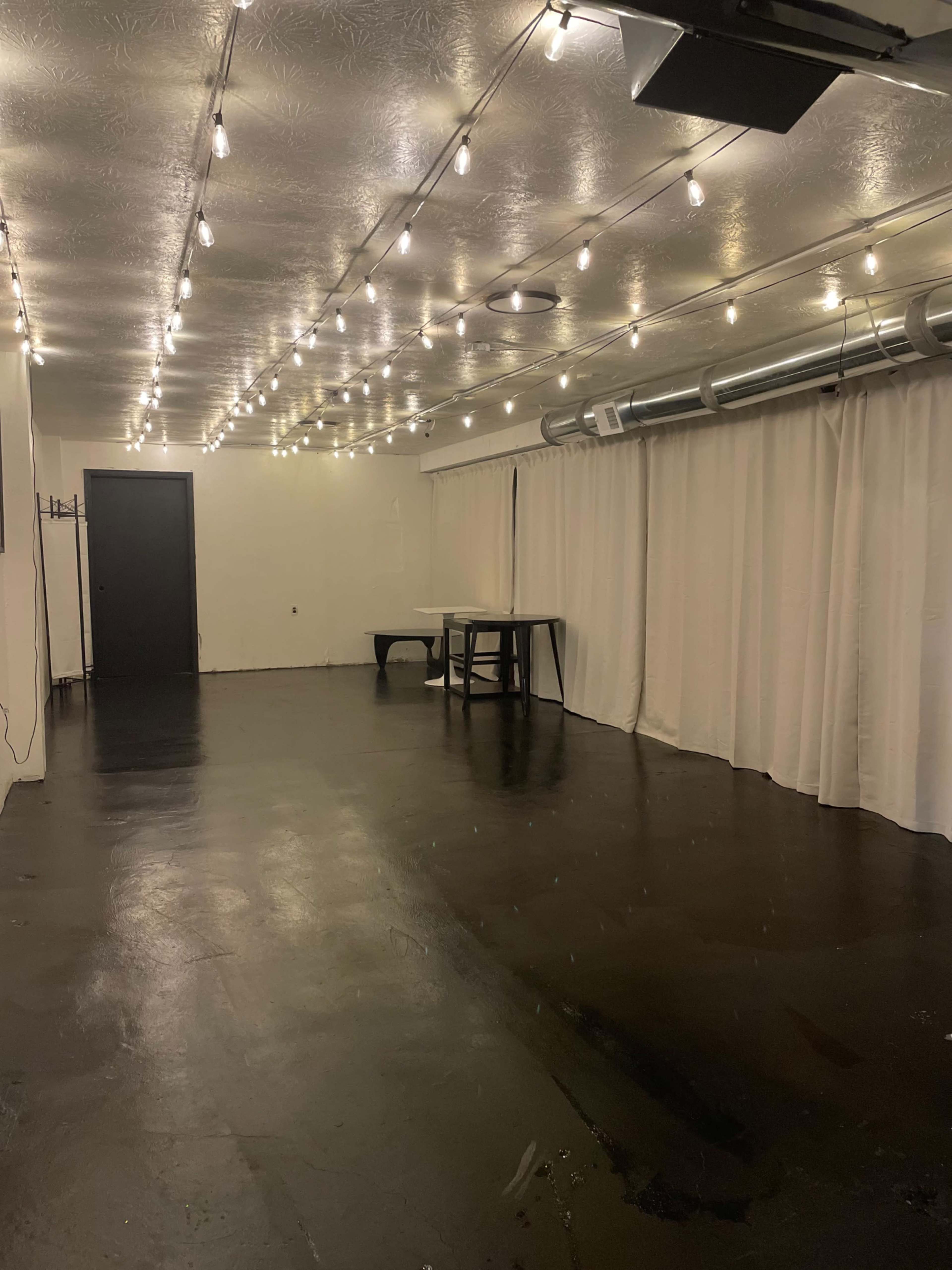 The image shows a spacious room with a dark floor, white walls, and overhead string lights illuminating the area.
