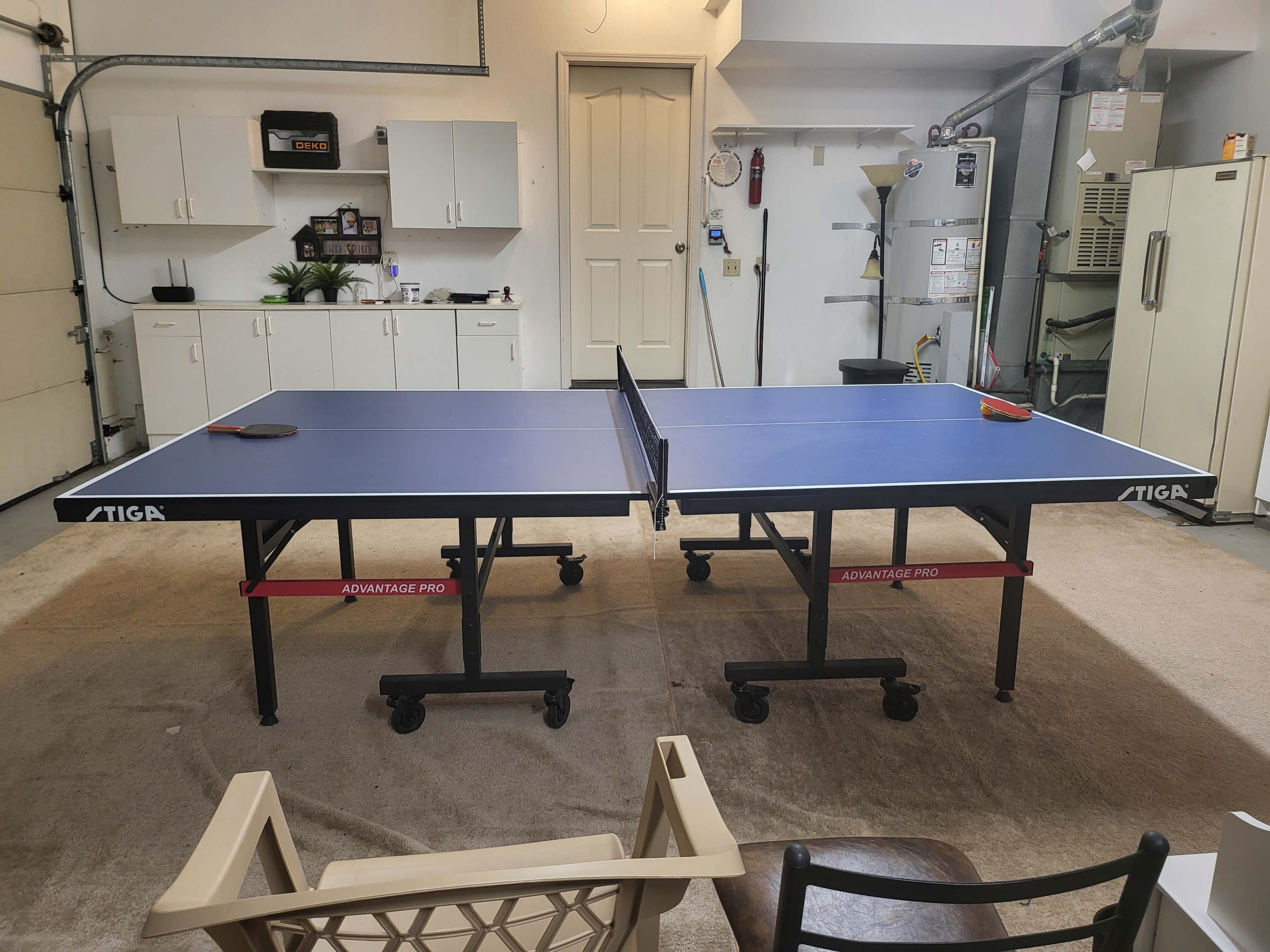 Two ping pong tables set up in a garage, with a chair and cabinets visible in the background.