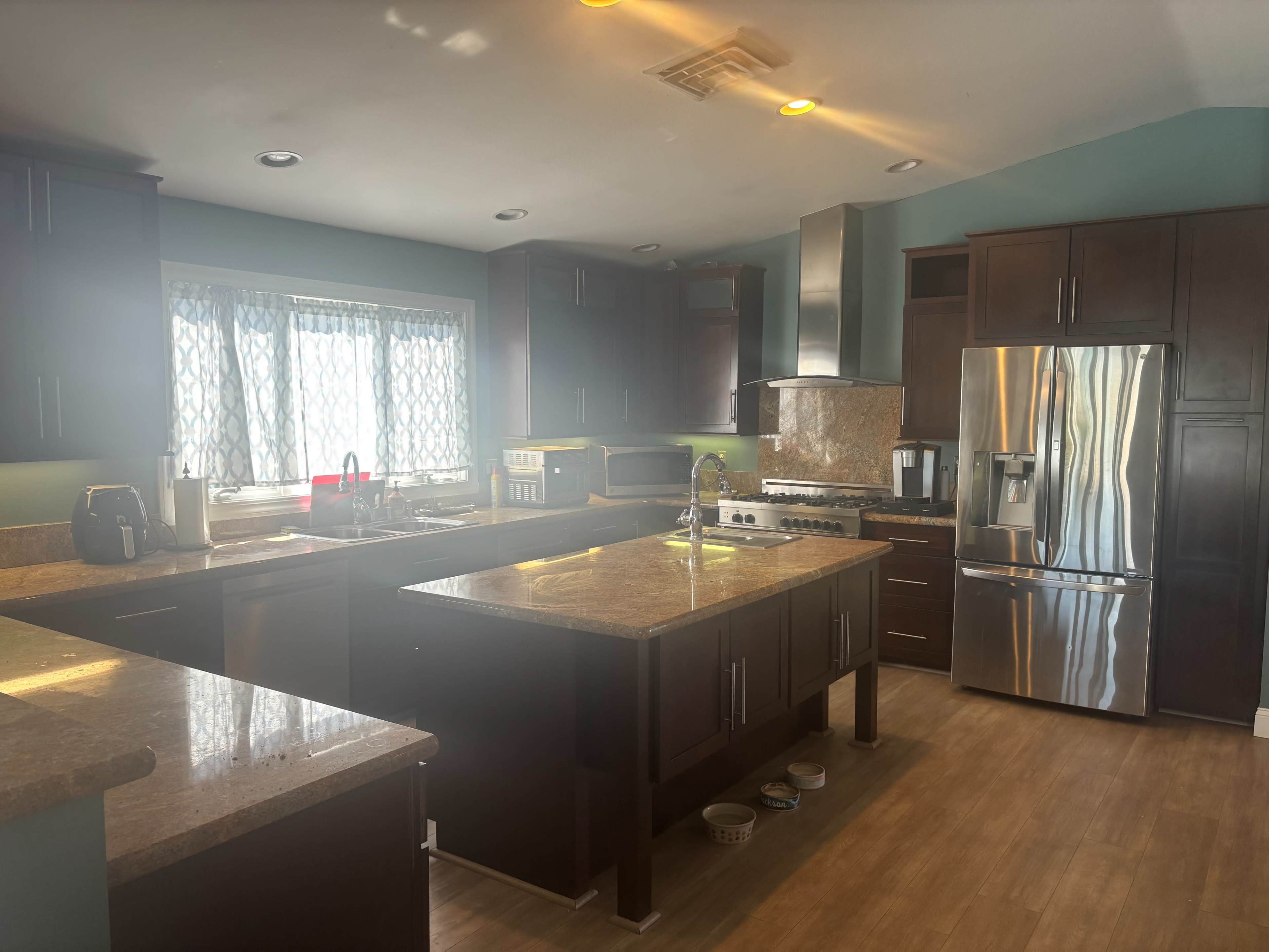 The image shows a modern kitchen featuring dark wooden cabinets, stainless steel appliances, and a large island with a granite countertop.