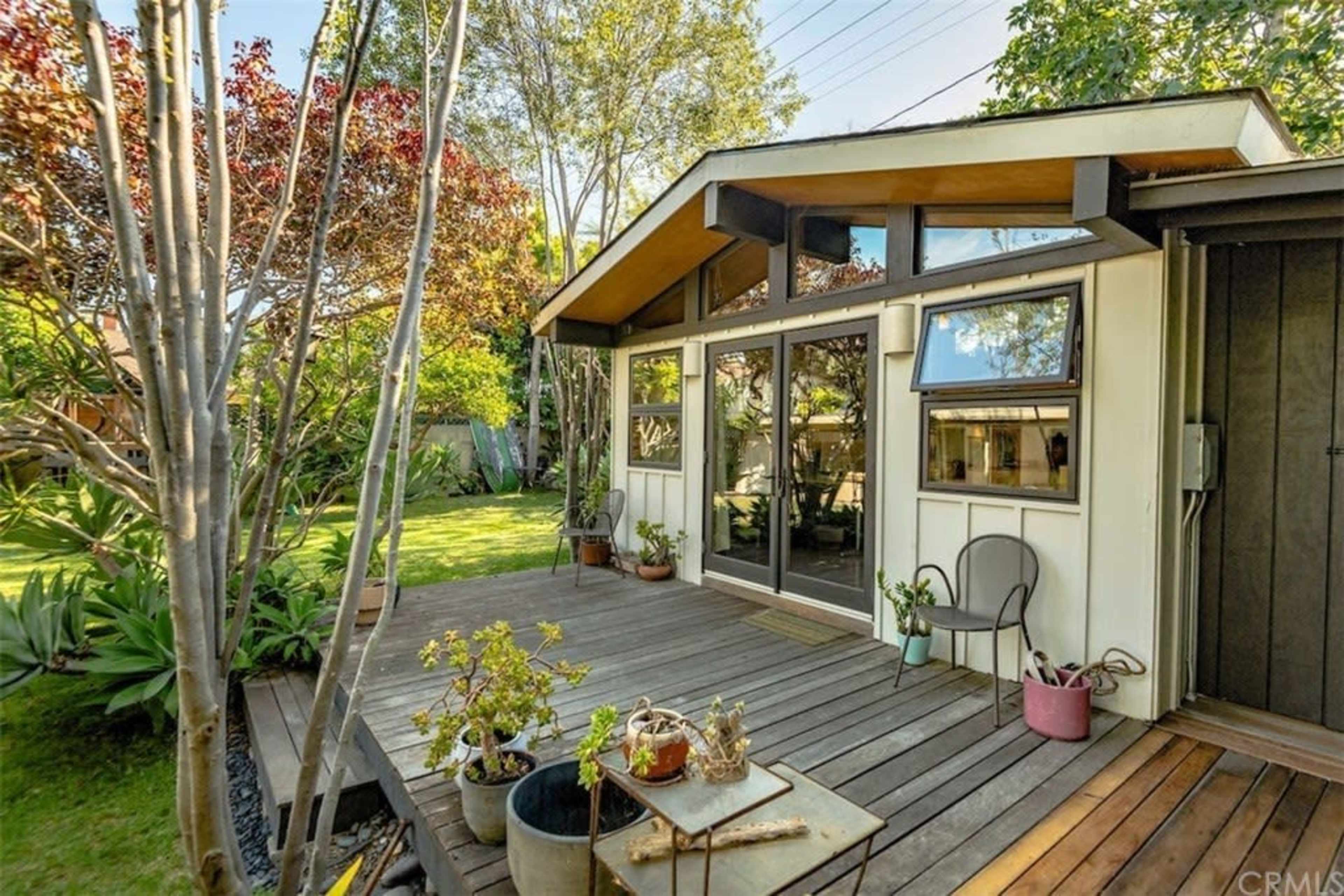 A wooden deck in front of a modern-style house surrounded by greenery and trees.