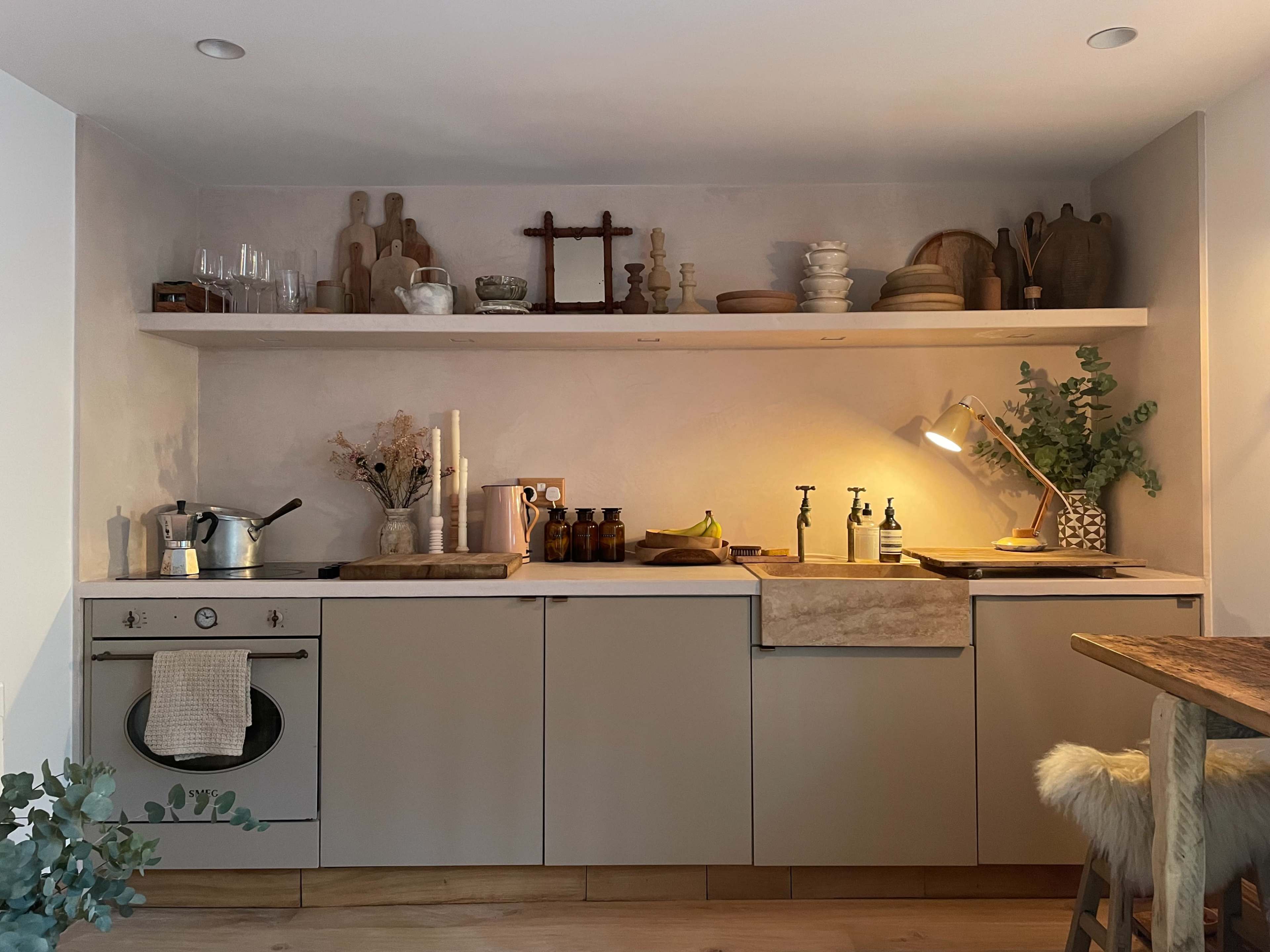 A modern kitchen features a minimalist design with a countertop, sink, and various utensils and decorative items arranged on shelves above.