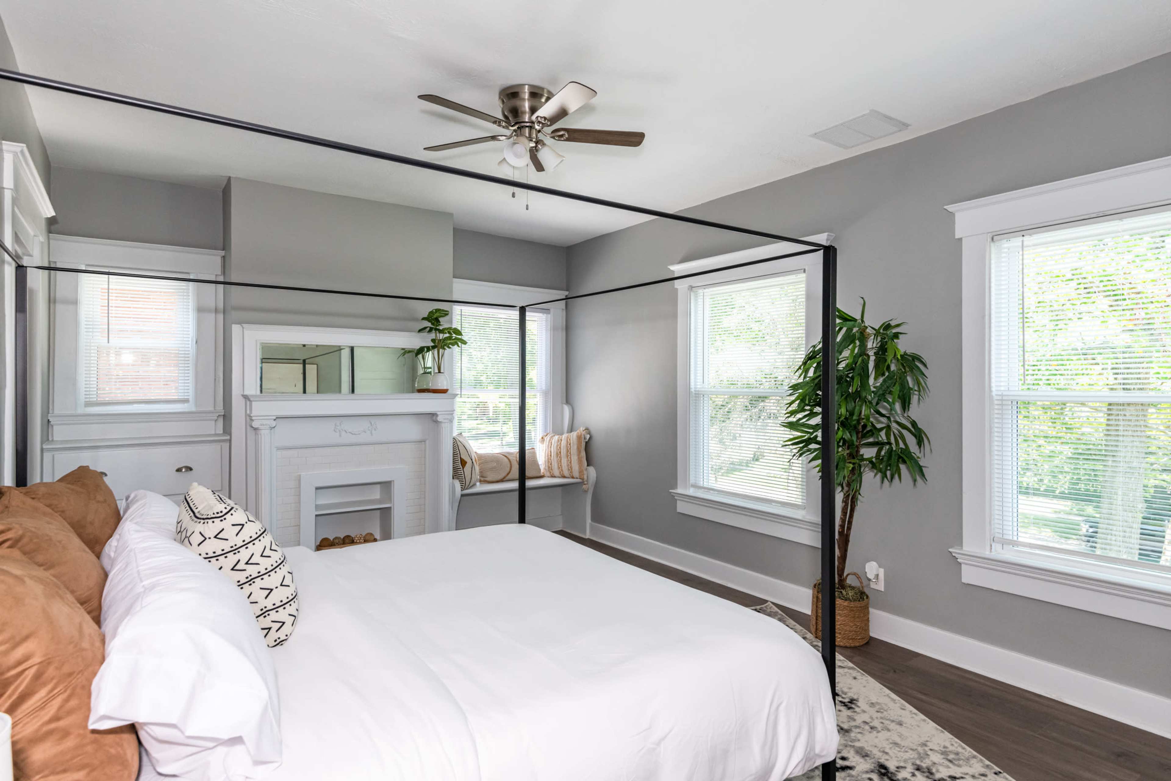 A minimalist bedroom features a four-poster bed, a cozy fireplace, and large windows allowing natural light to fill the space.