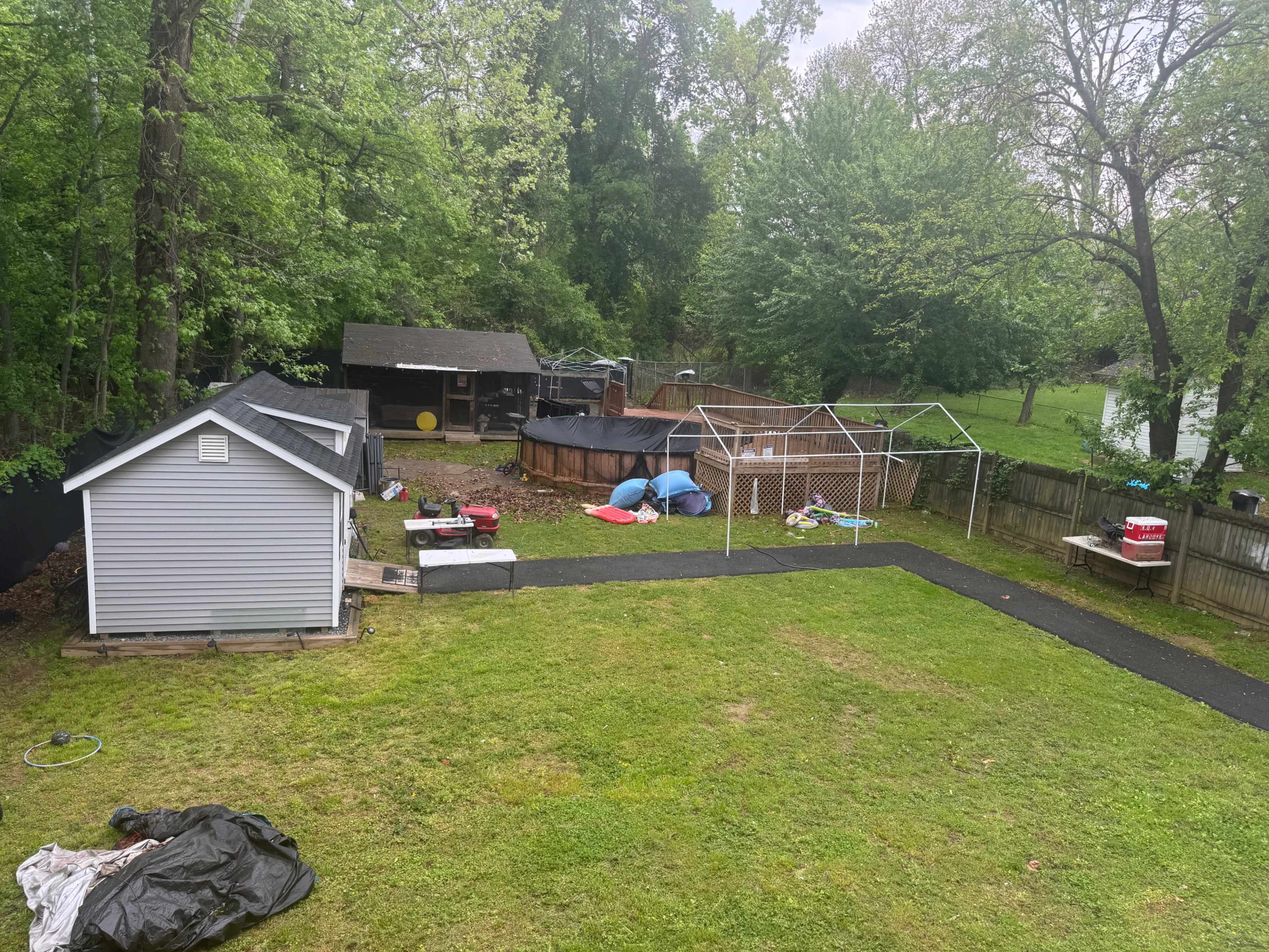 The image shows a backyard featuring a storage shed, a large above-ground pool, a gazebo structure, and various outdoor items scattered across the green lawn.