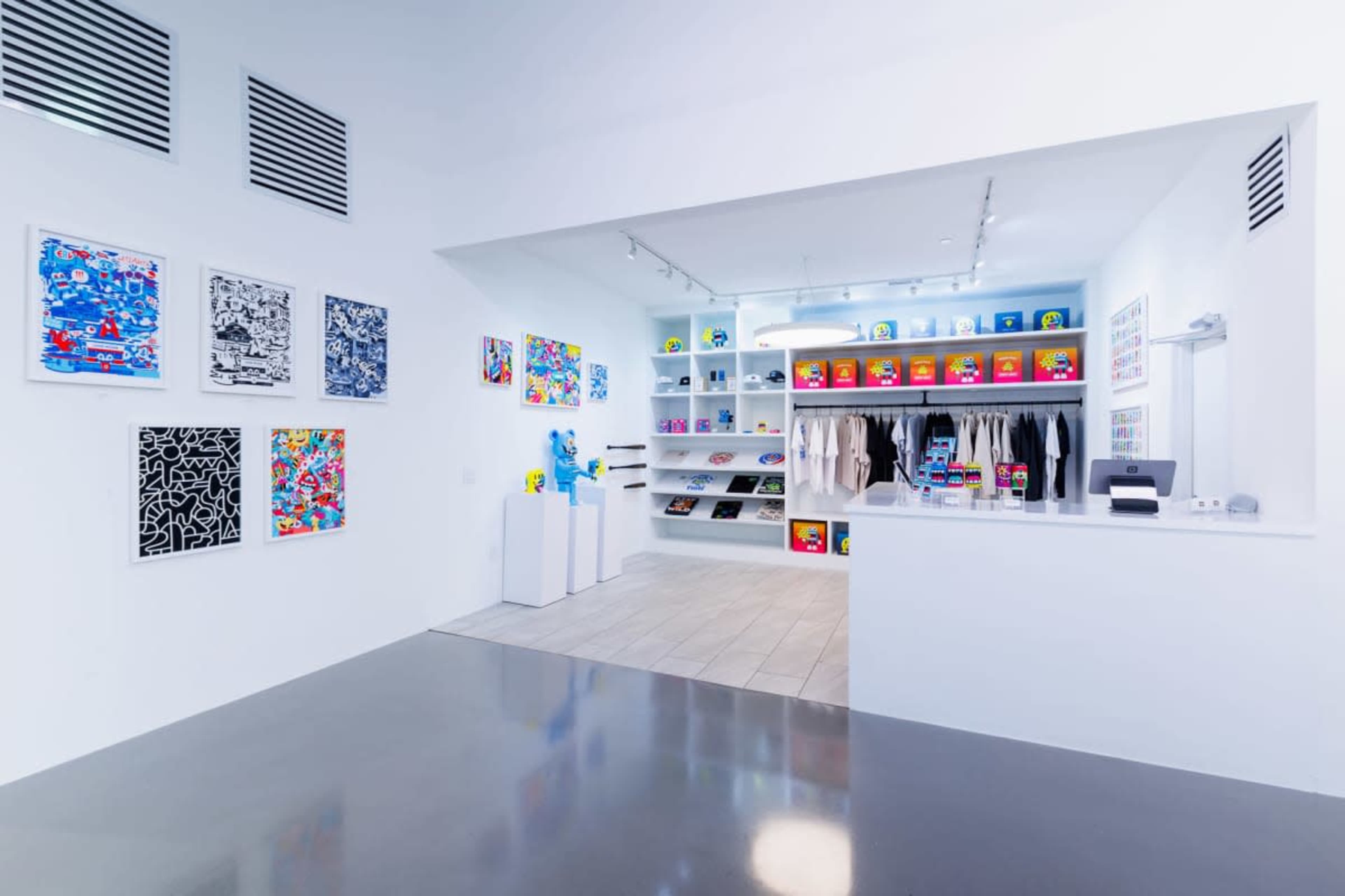 The image shows a modern retail space featuring colorful artwork on the walls and a display area with various clothing and merchandise items organized on shelves.