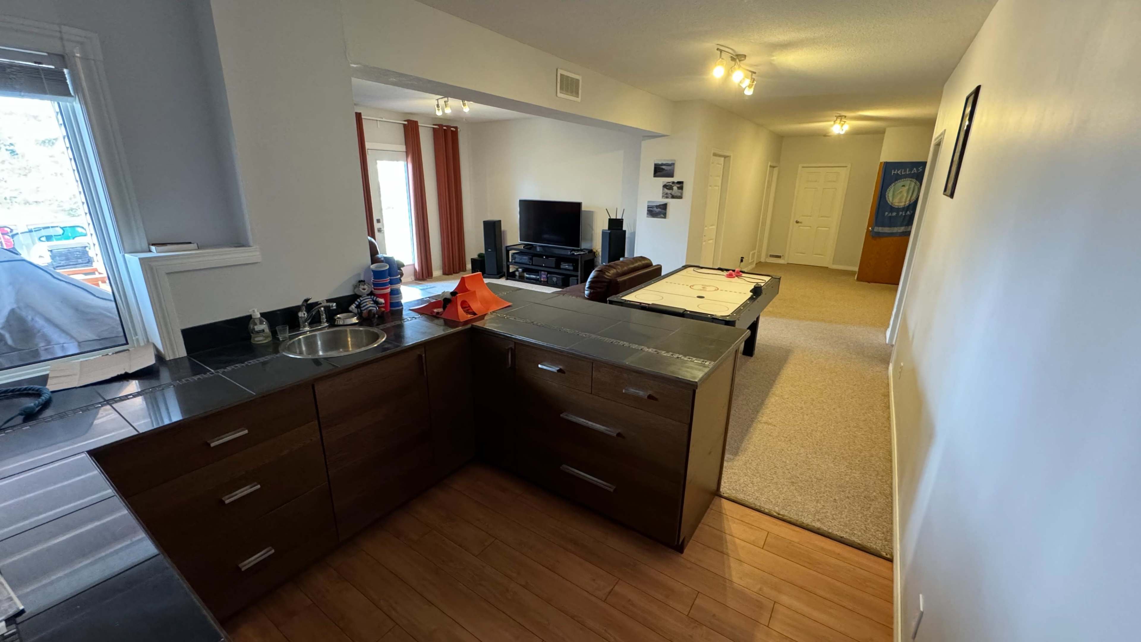 An open-plan living area with a kitchen on the left and a living room area featuring a TV and a pool table in the background.