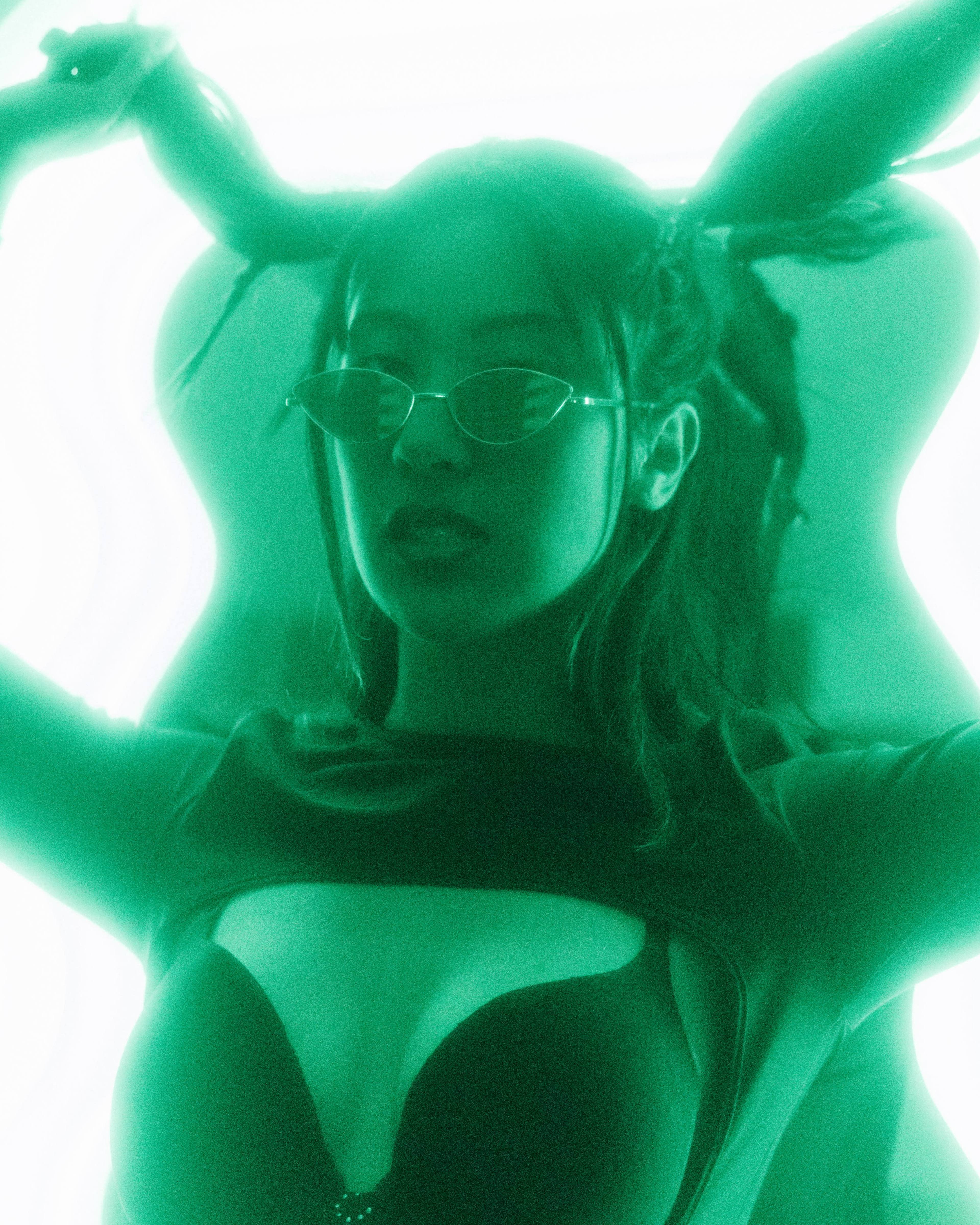 A woman poses with her hair pulled back while wearing sunglasses against a glowing green background.