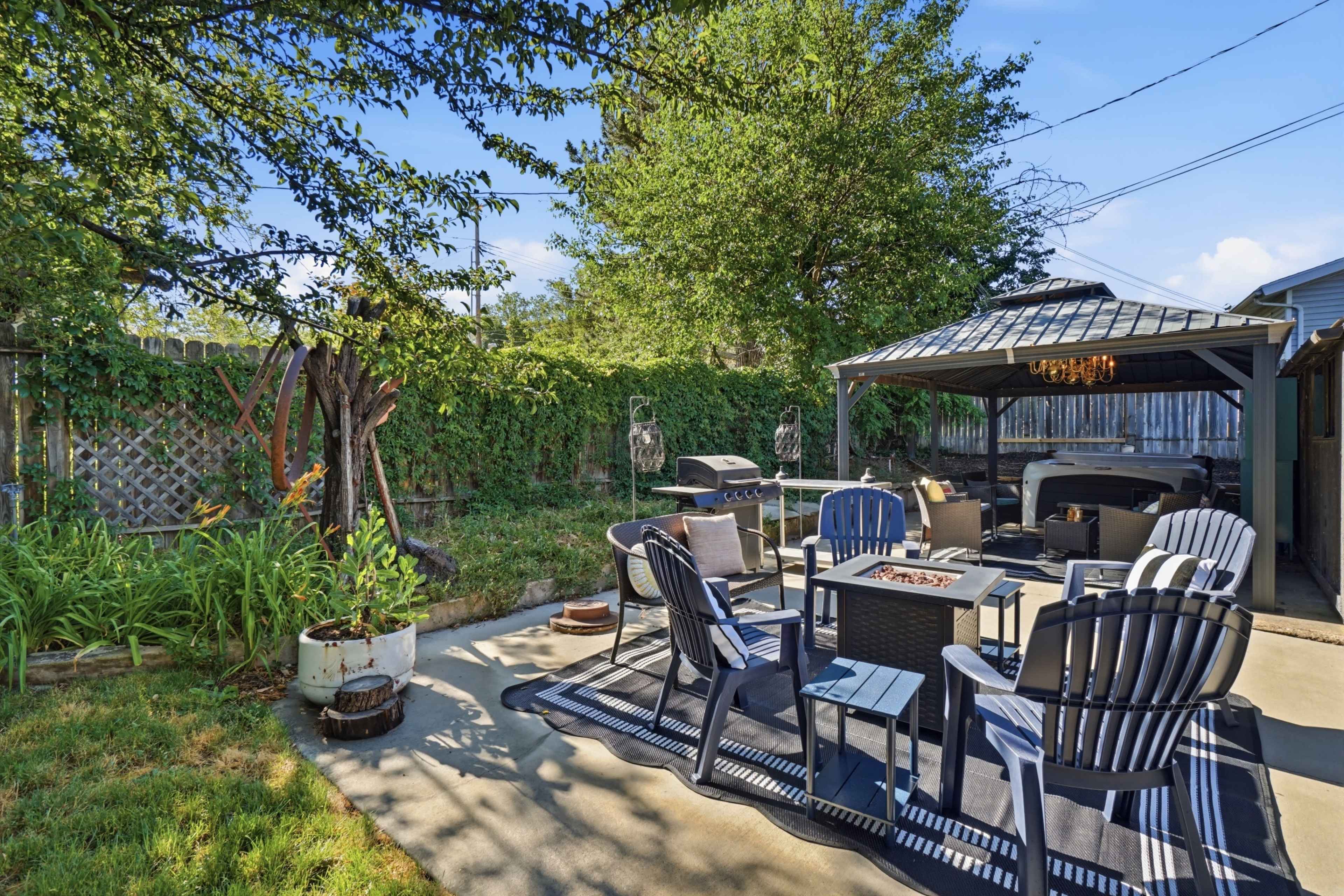 The image shows a patio area with a gazebo, seating arrangements around a table, a grill, and landscaped greenery in the background.