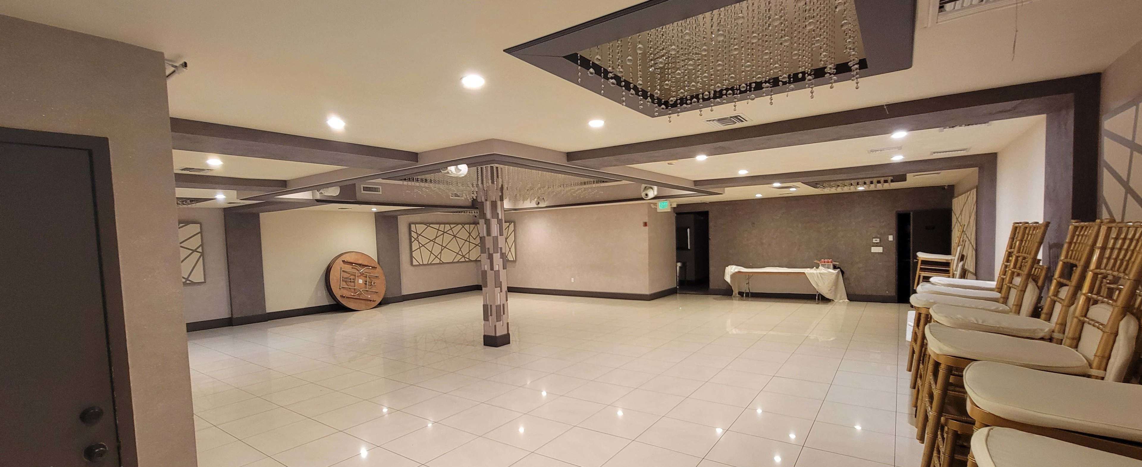 The image shows an empty event hall with white tiled flooring, beige walls, and a chandelier hanging from the ceiling.