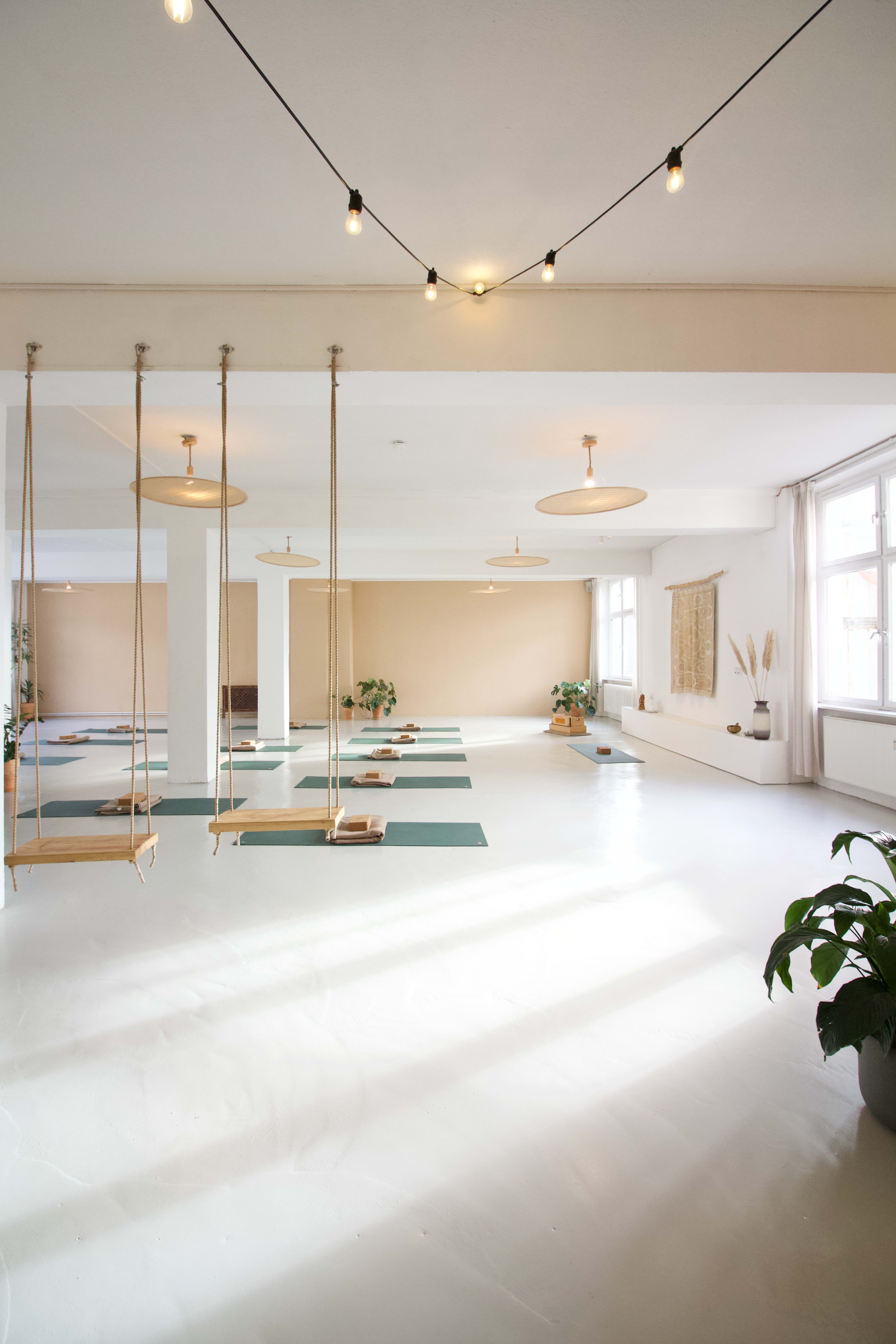 A spacious, well-lit room with yoga mats arranged on the floor and swings hanging from the ceiling.
