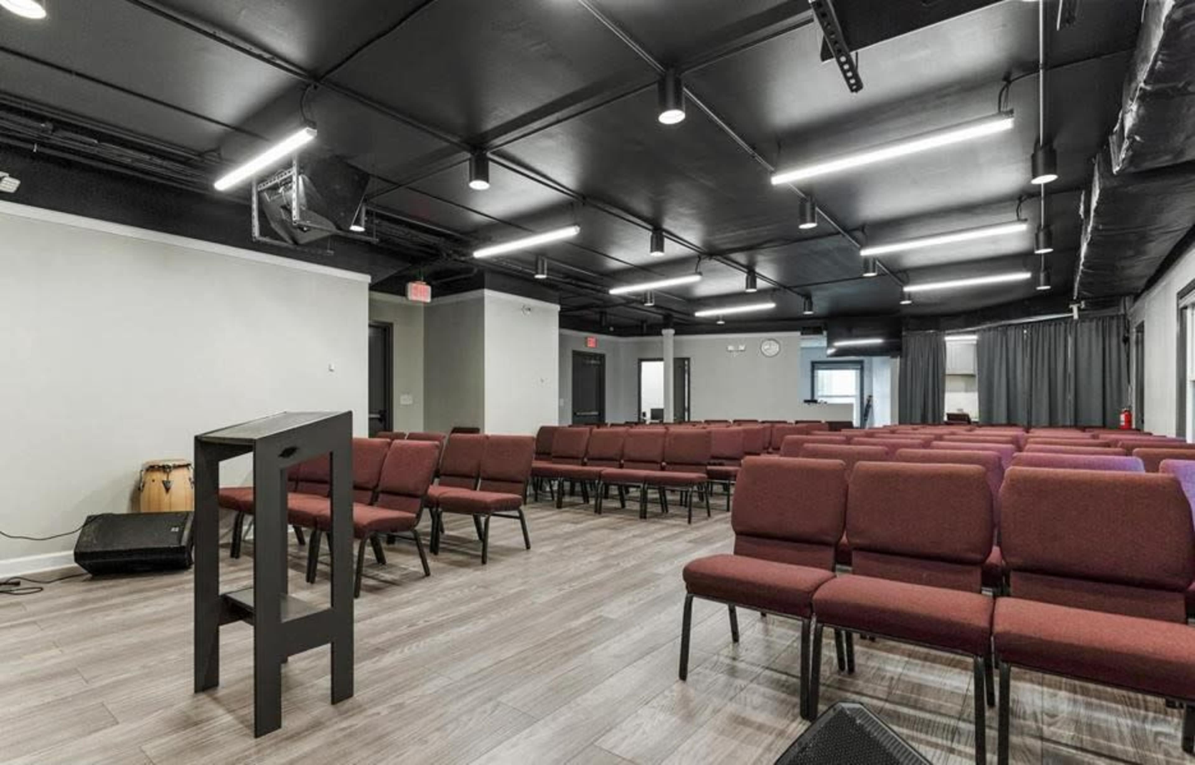 A spacious meeting room features rows of maroon chairs and a small platform at the front.