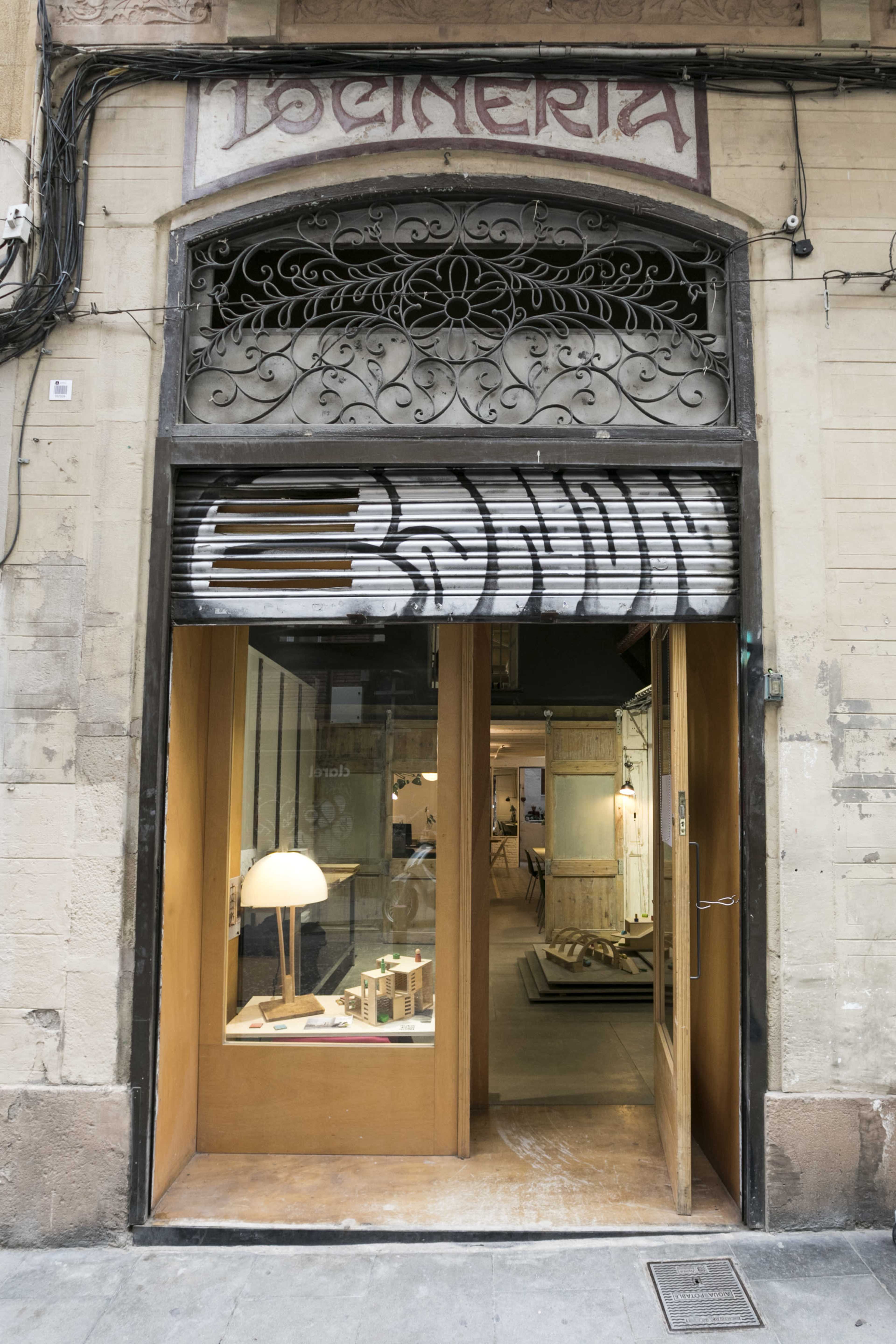 The entrance of a shop with a decorative sign above and a display of wooden items visible through the glass door.