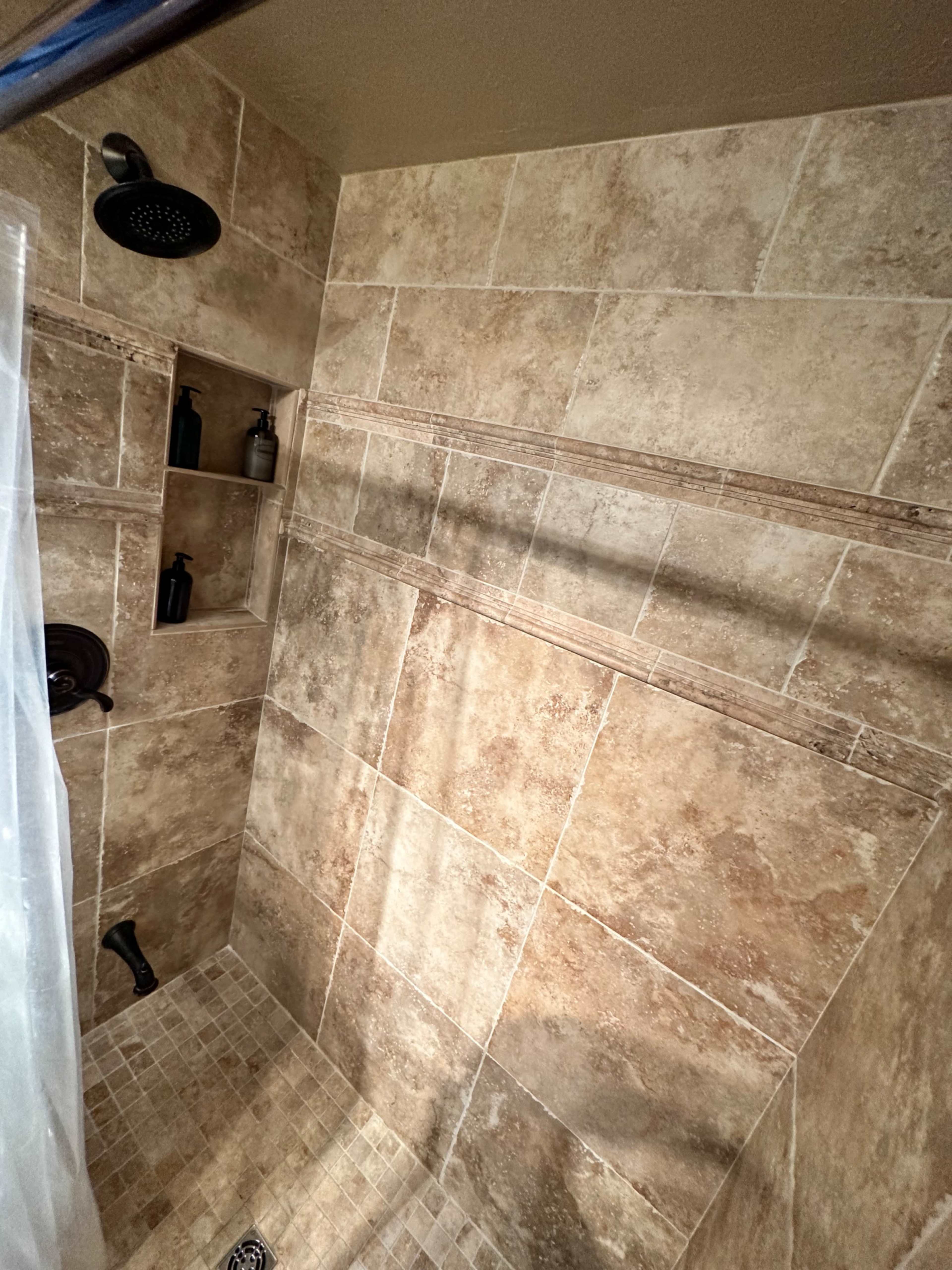 A tiled shower with built-in shelves for toiletries and a rainfall showerhead.
