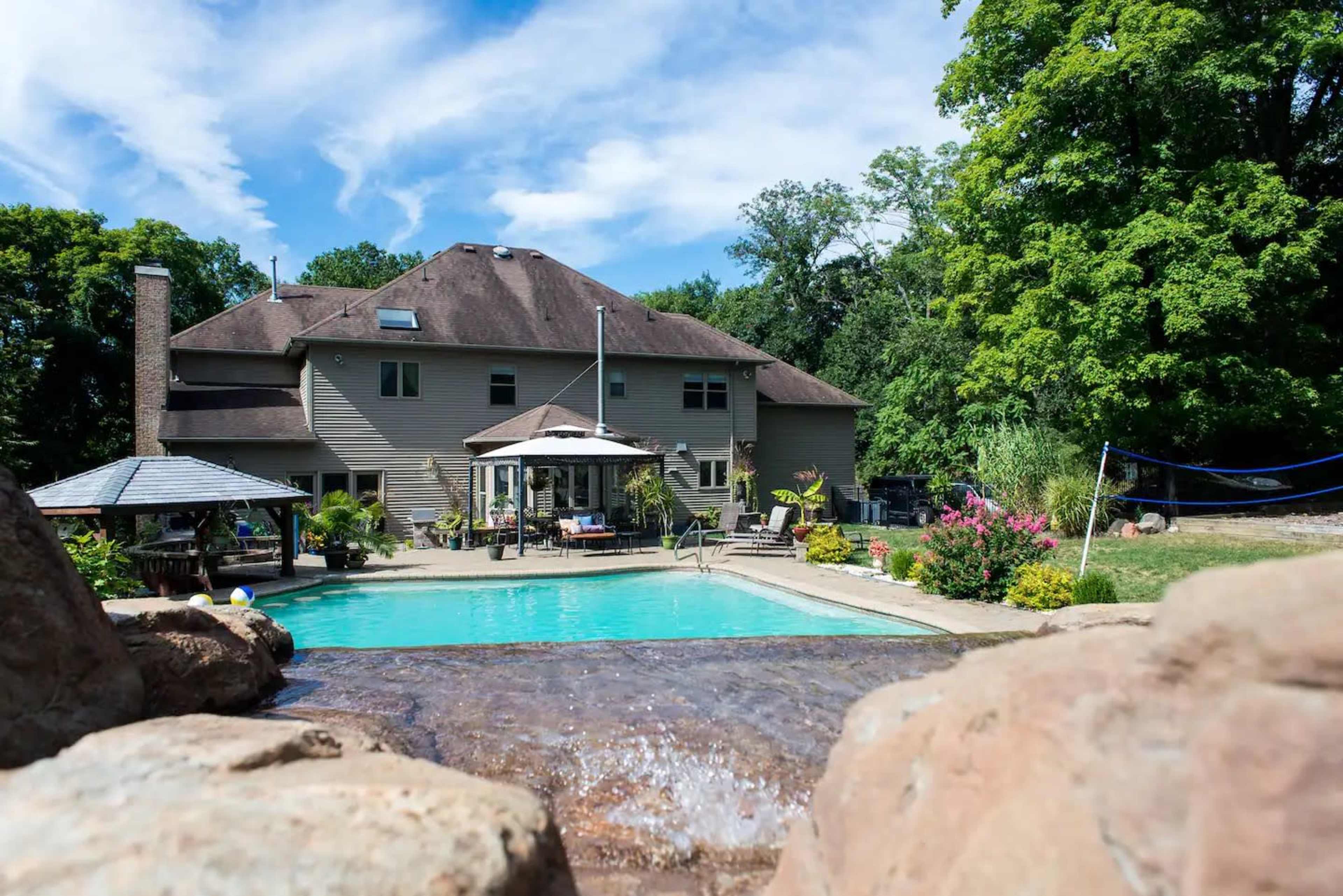 A large house with a backyard swimming pool, surrounded by greenery and outdoor seating areas.