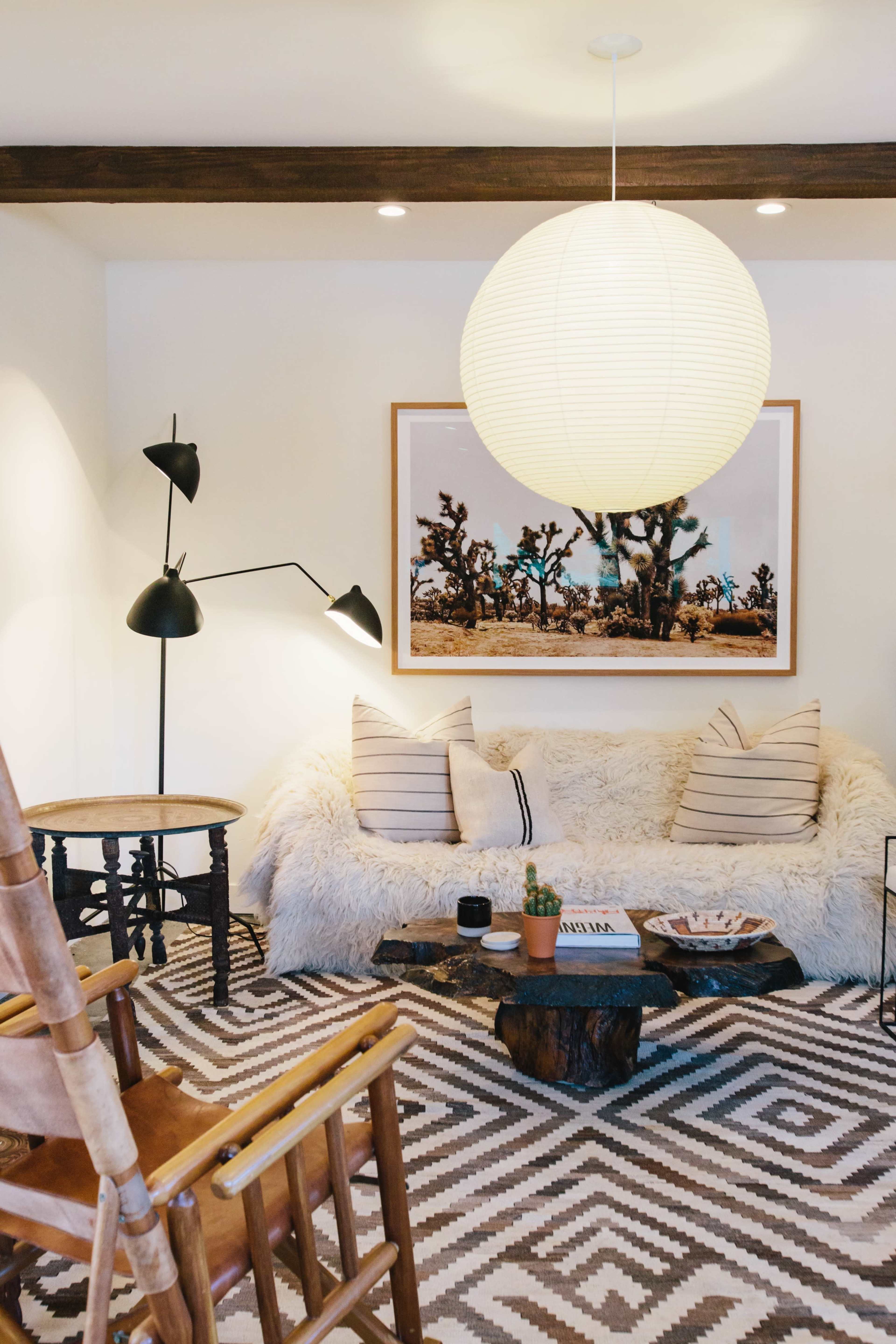 The living room features a fur-covered sofa, a round paper lamp hanging from the ceiling, and a patterned rug, with a wooden coffee table and a rocking chair.