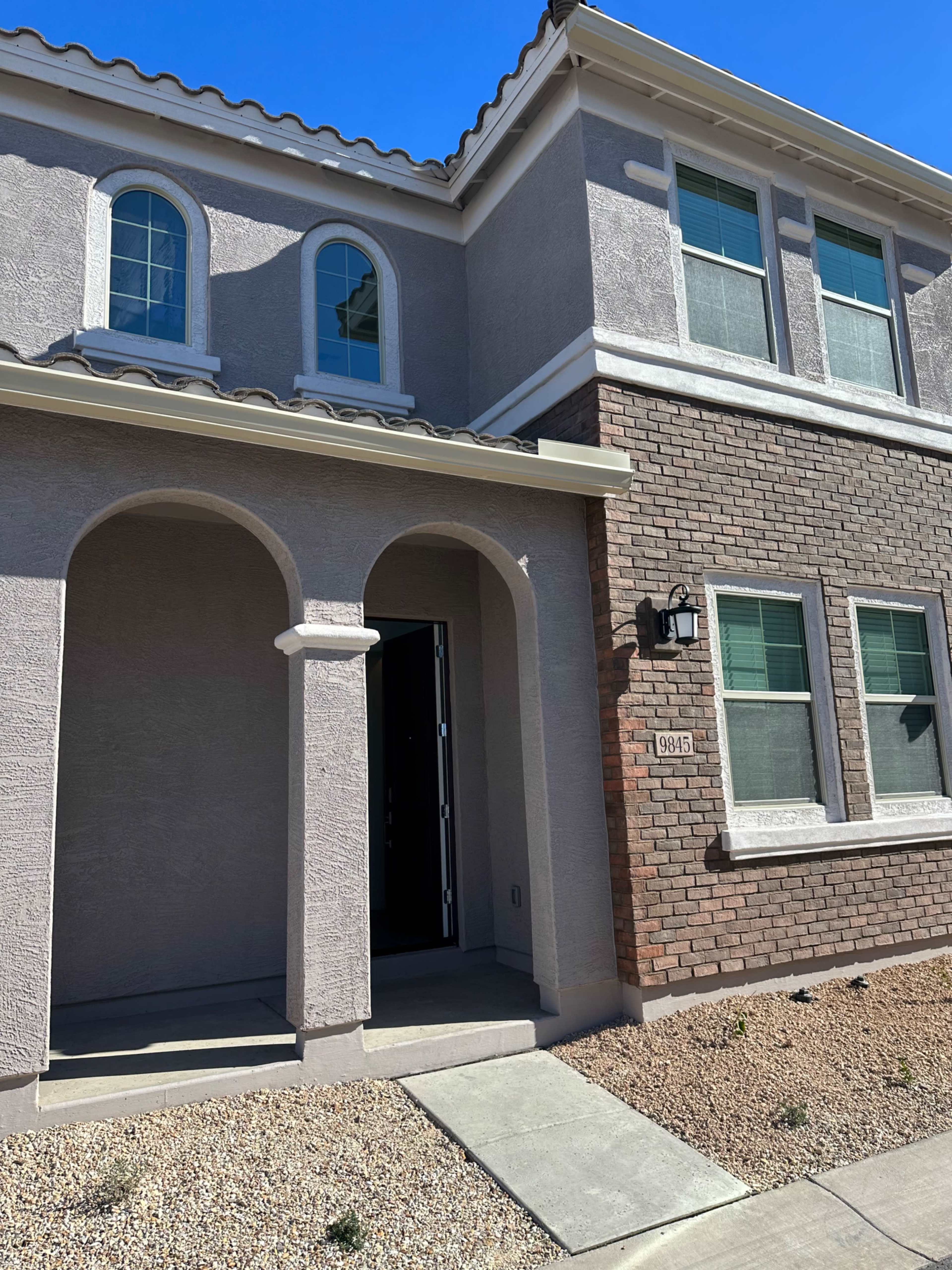 The entrance of a two-story house featuring a combination of gray stucco and brick exterior, with a covered porch and a prominent front door.