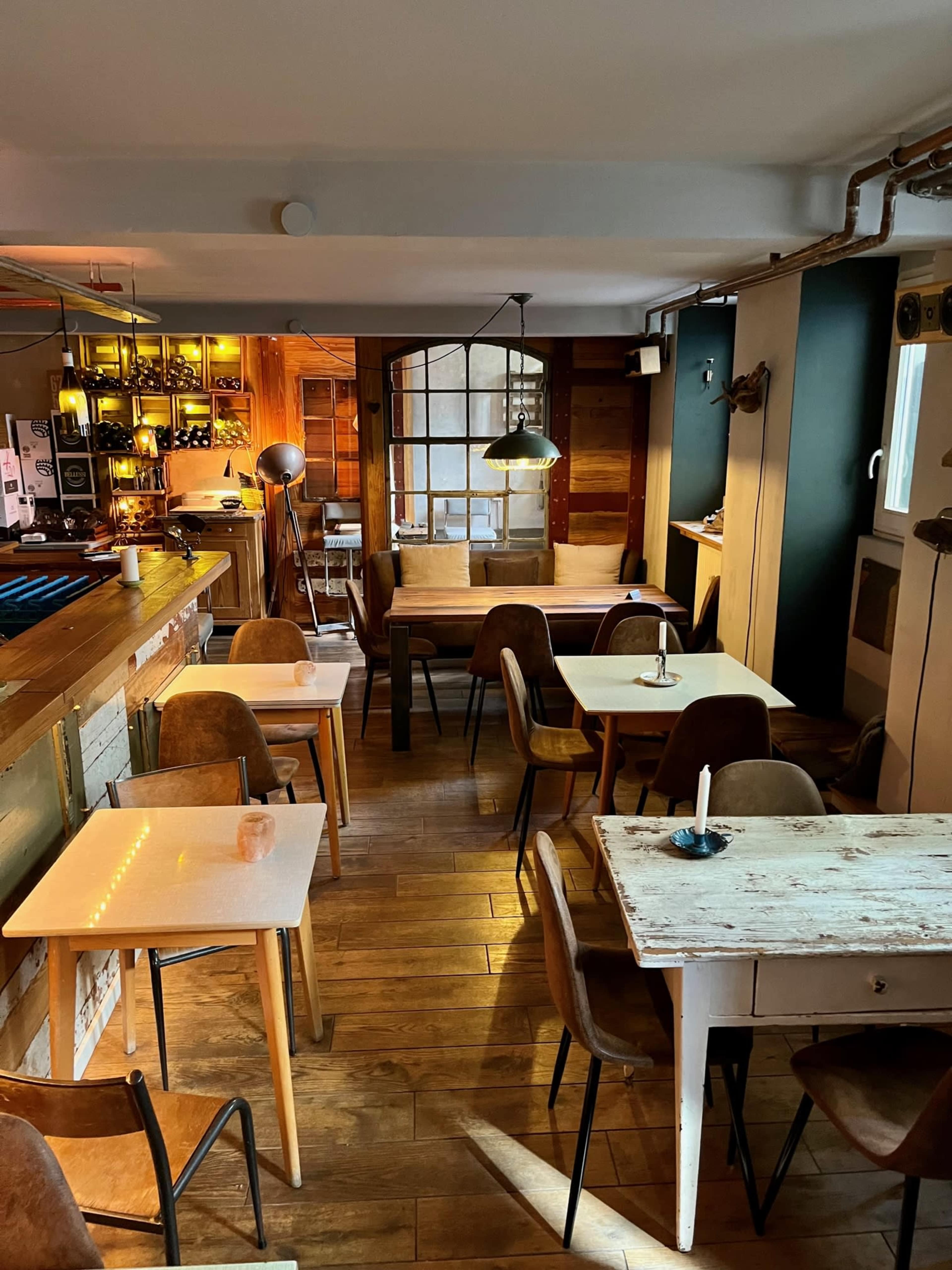 A cozy café interior with wooden floors, various tables, and warm lighting.
