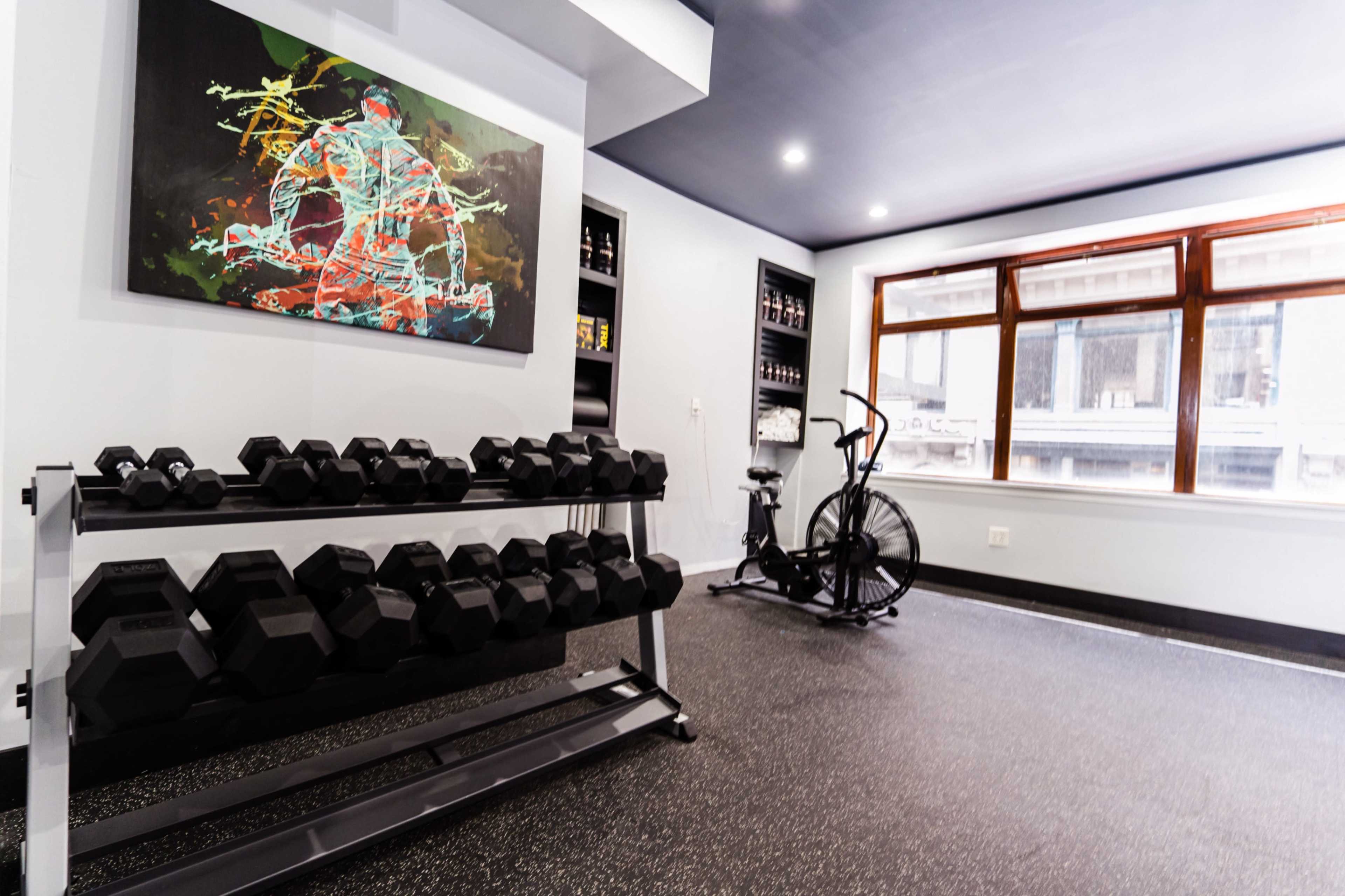 A modern home gym with a rack of dumbbells, an exercise bike, and a colorful abstract painting on the wall.