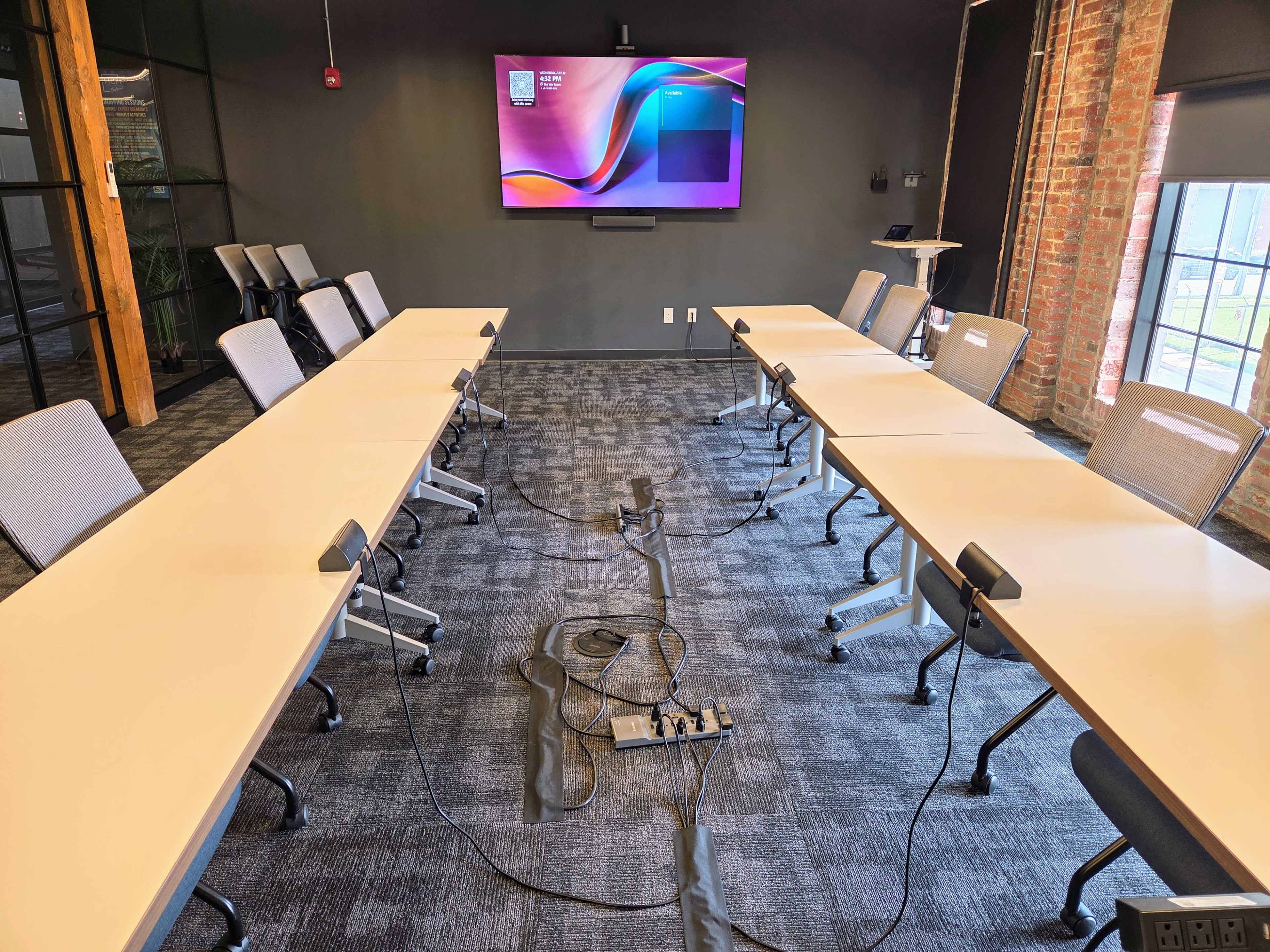 The image shows a modern conference room with eight tables arranged in a U-shape, equipped with microphones, and a large screen mounted on the wall at the front.