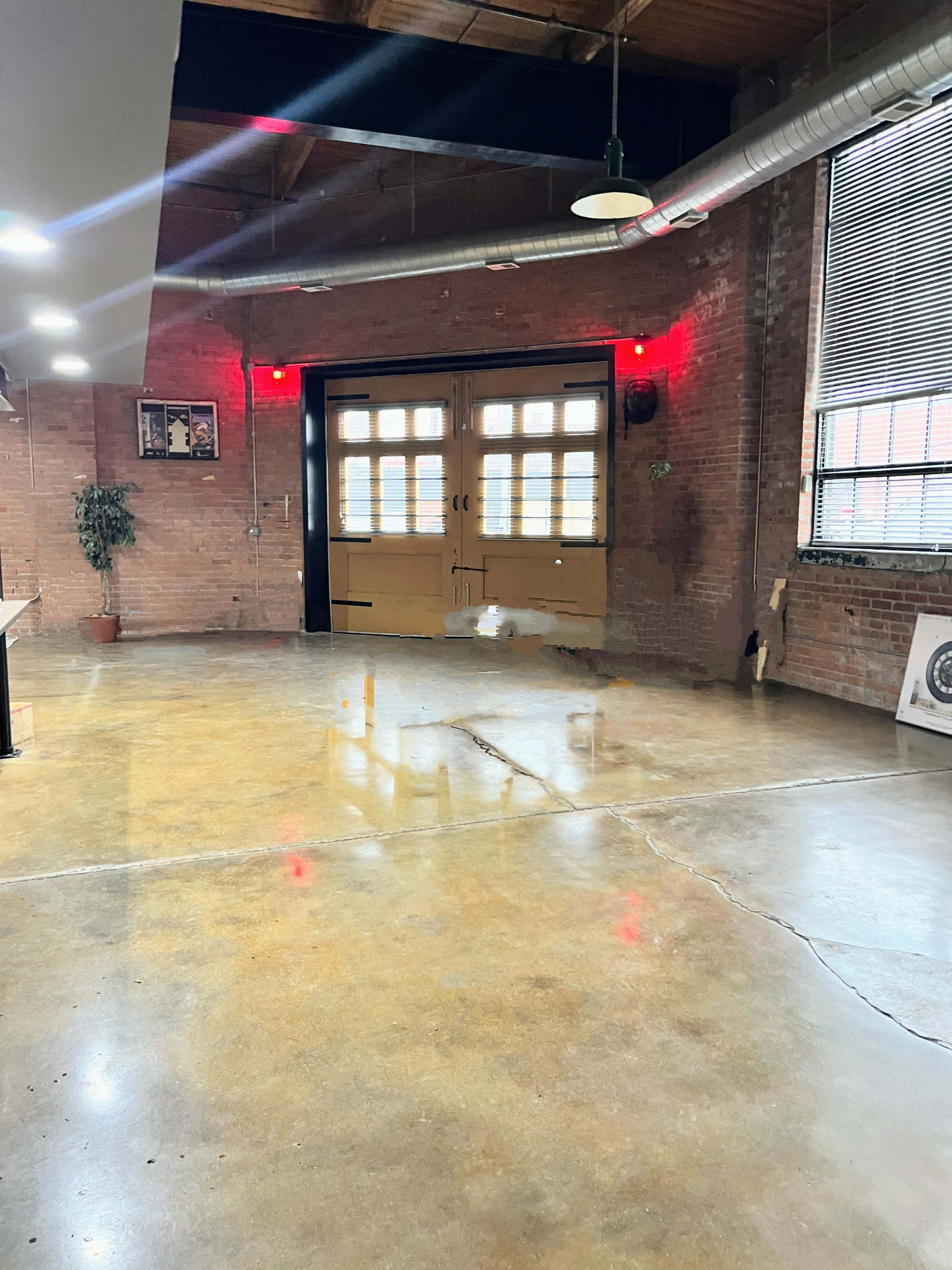 An industrial-style room with a polished concrete floor, exposed brick walls, and large double doors at one end.