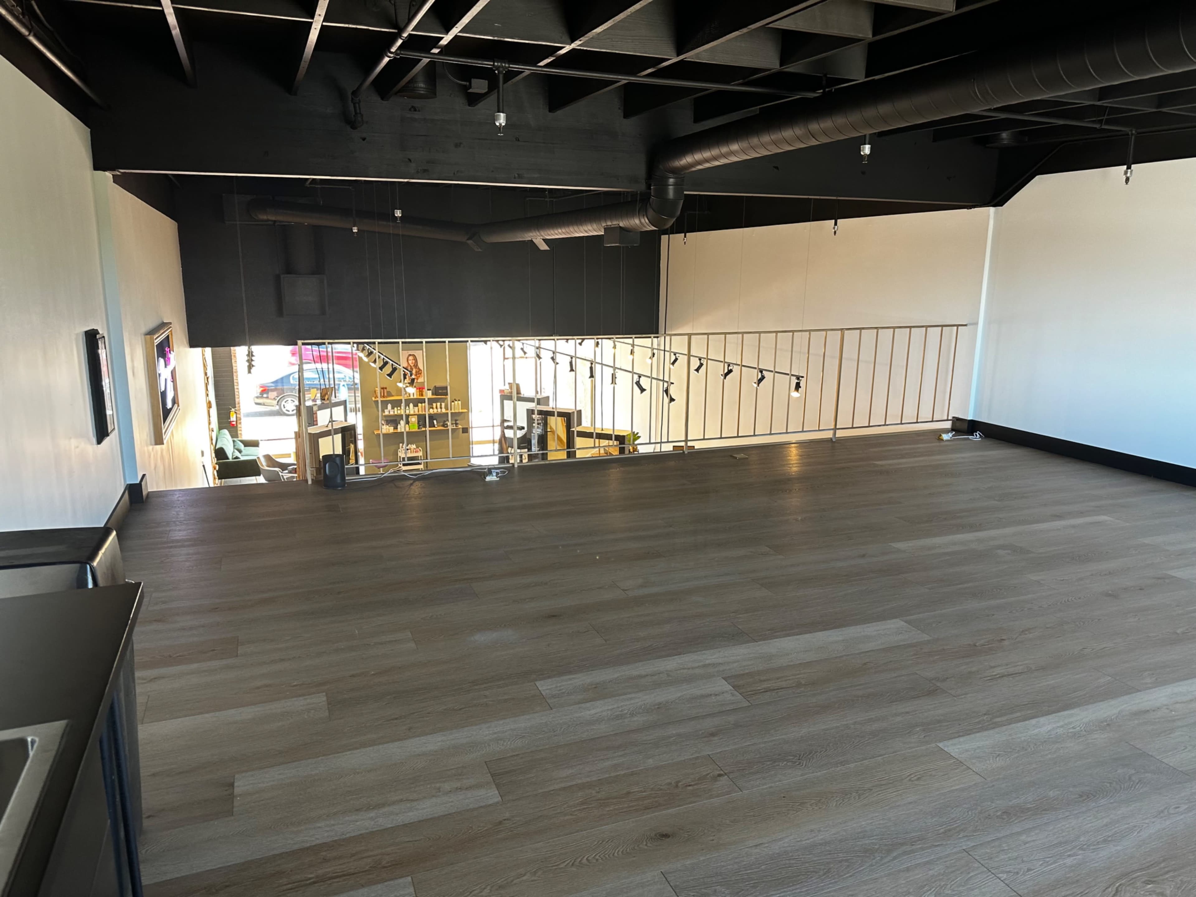 A spacious, empty room with light-colored wooden flooring and a railing overlooking a lower level.