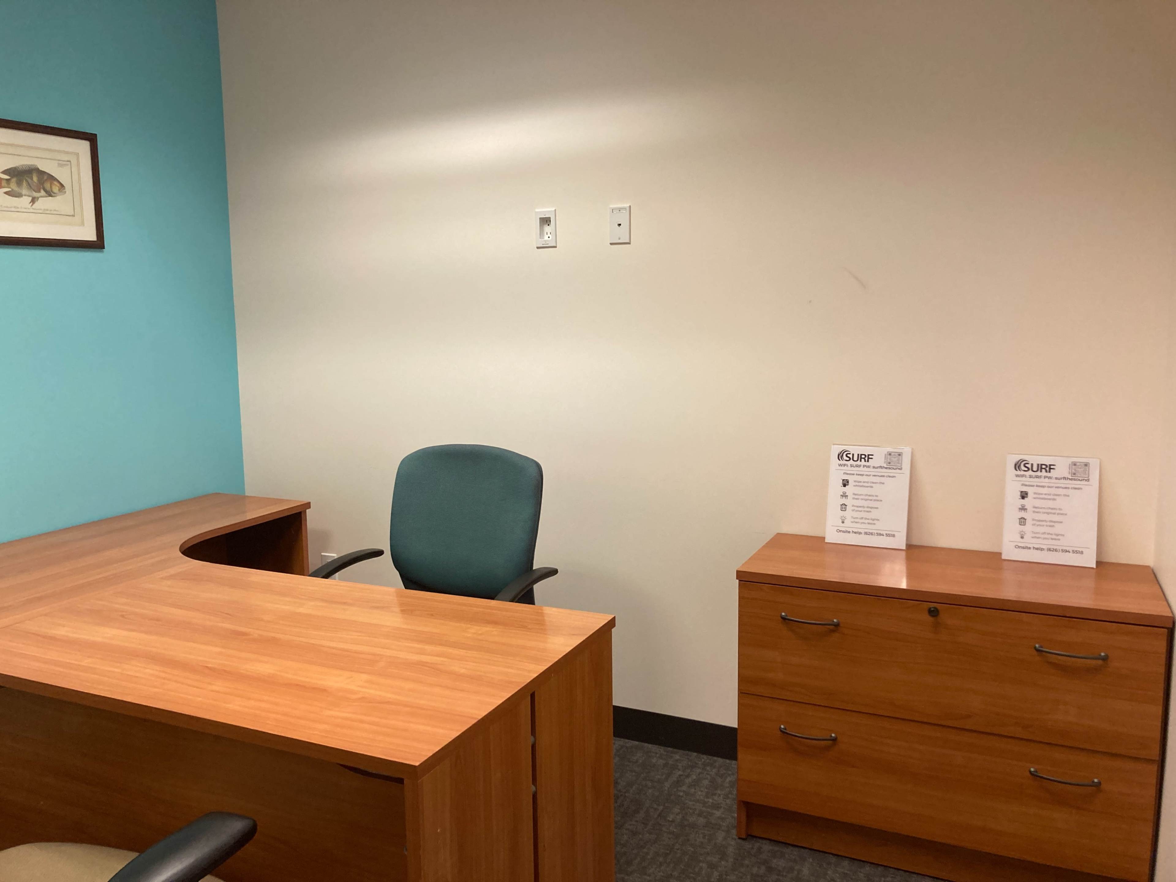 A vacant office with a wooden desk, a teal chair, and two file cabinets next to informational flyers on the desk.