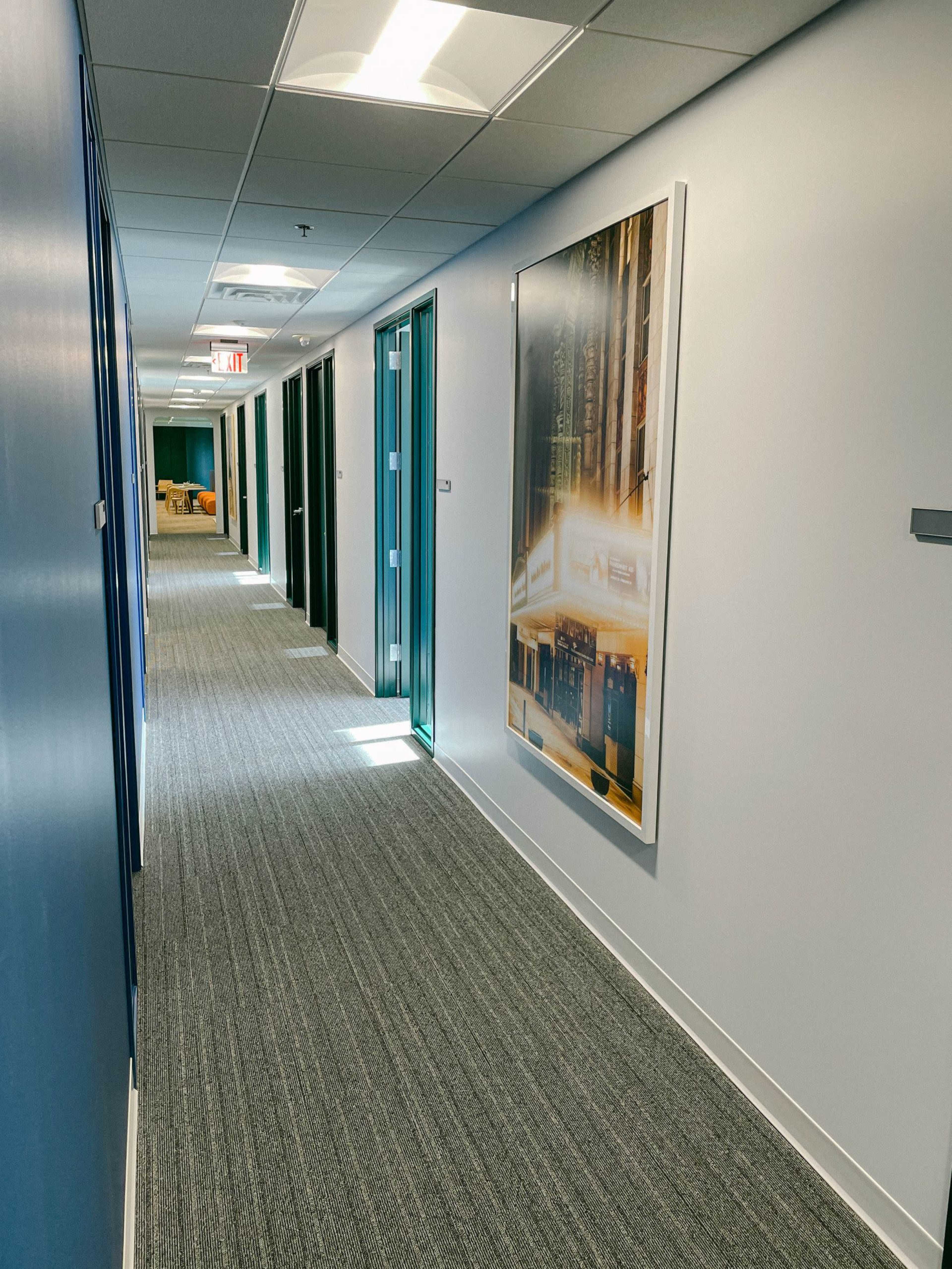 A wide hallway with several closed office doors on either side and a large framed photograph on the wall.