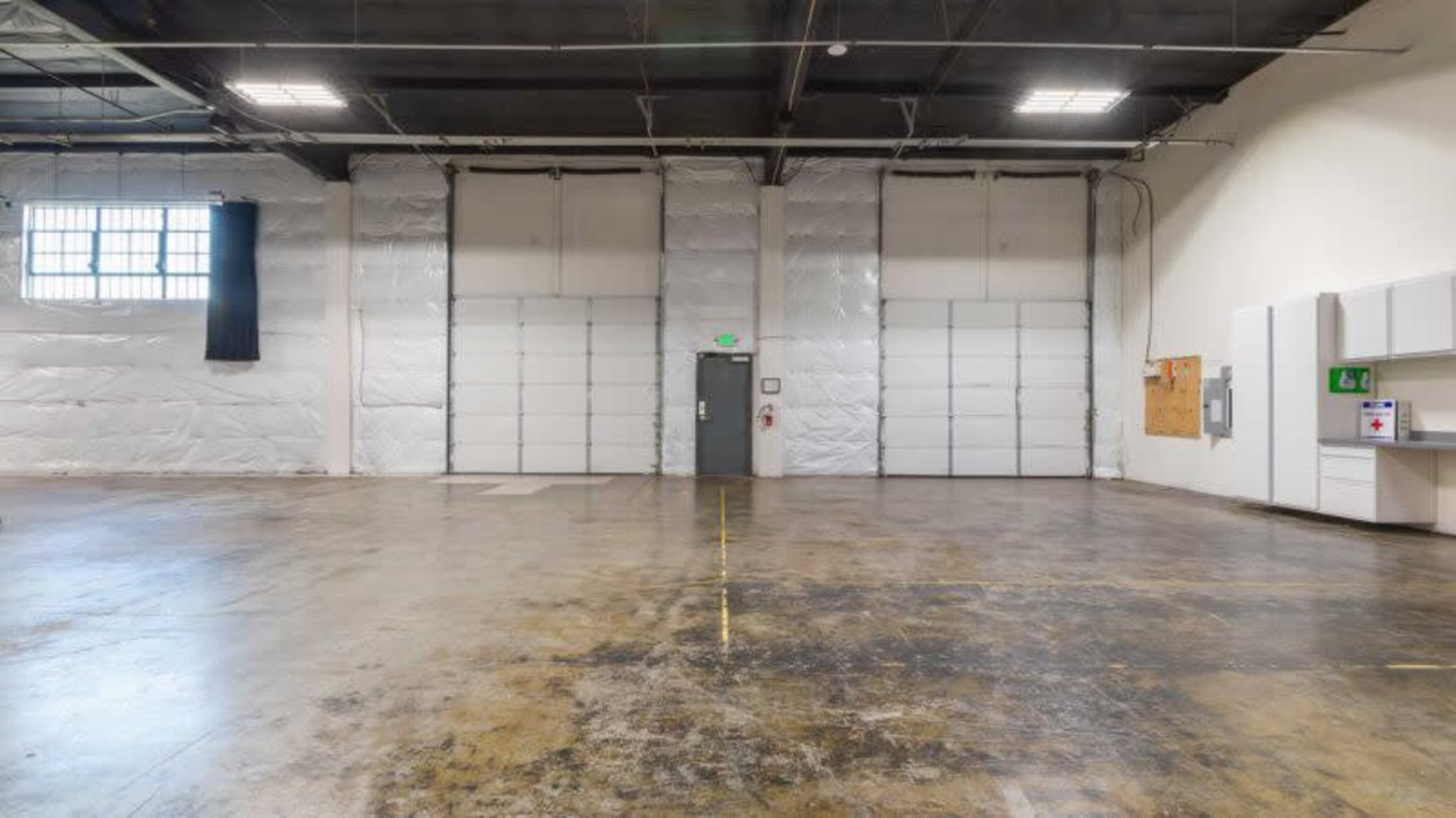 A large, empty industrial warehouse space with high ceilings and two large roll-up doors on one side.
