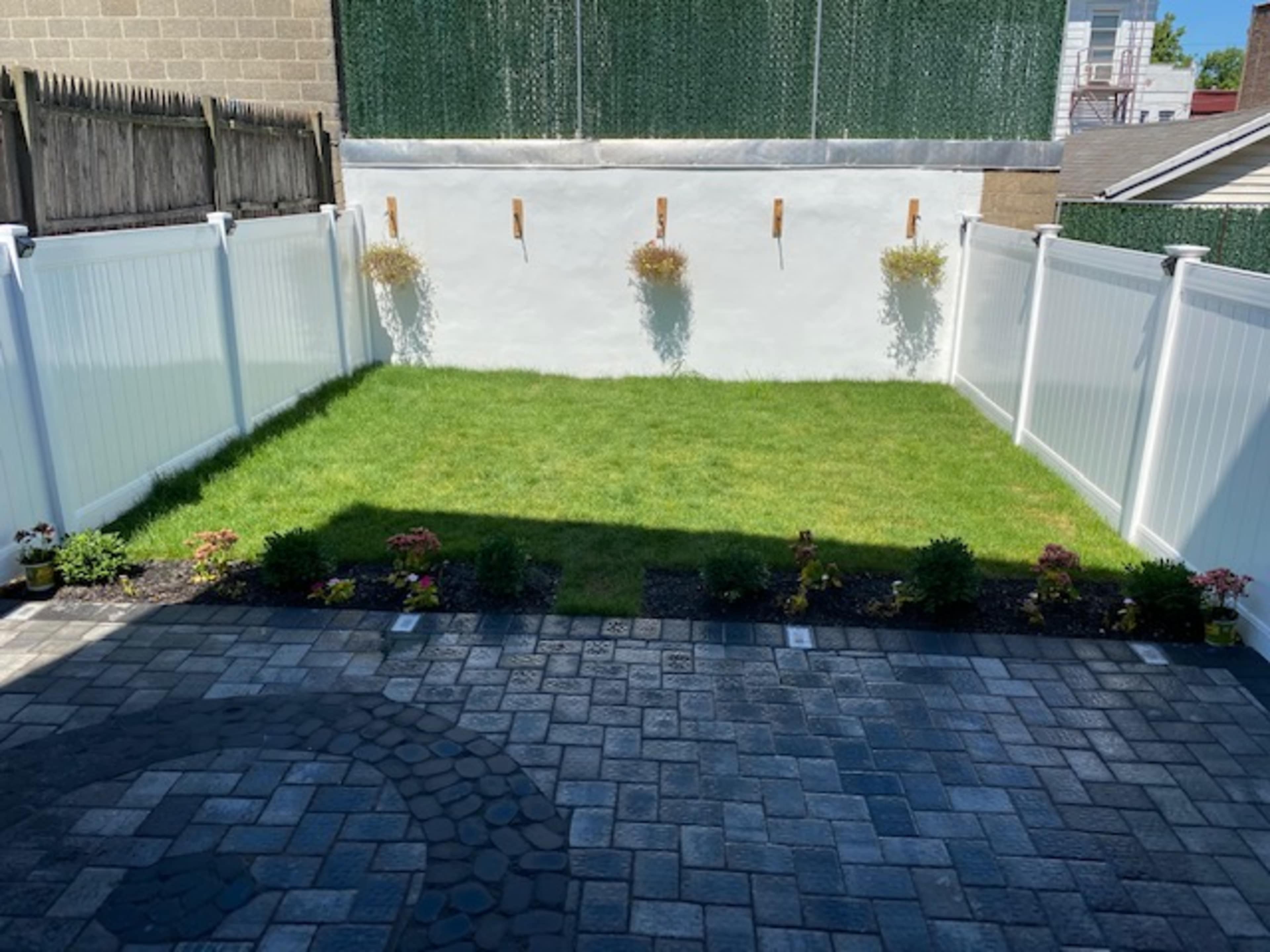 A fenced backyard with neatly arranged grass and flower beds along the perimeter.