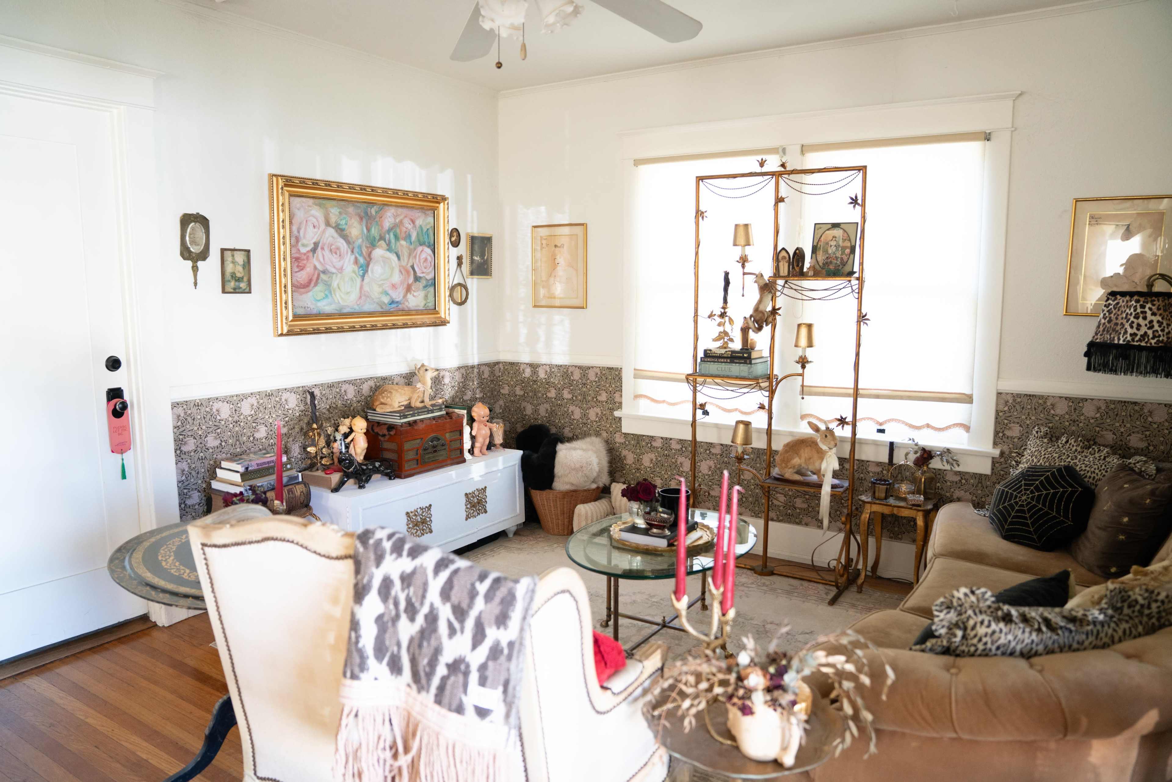 The image shows a cozy living room with a mix of decorative artwork, a vintage chest, plush seating, and various decorative items arranged throughout.