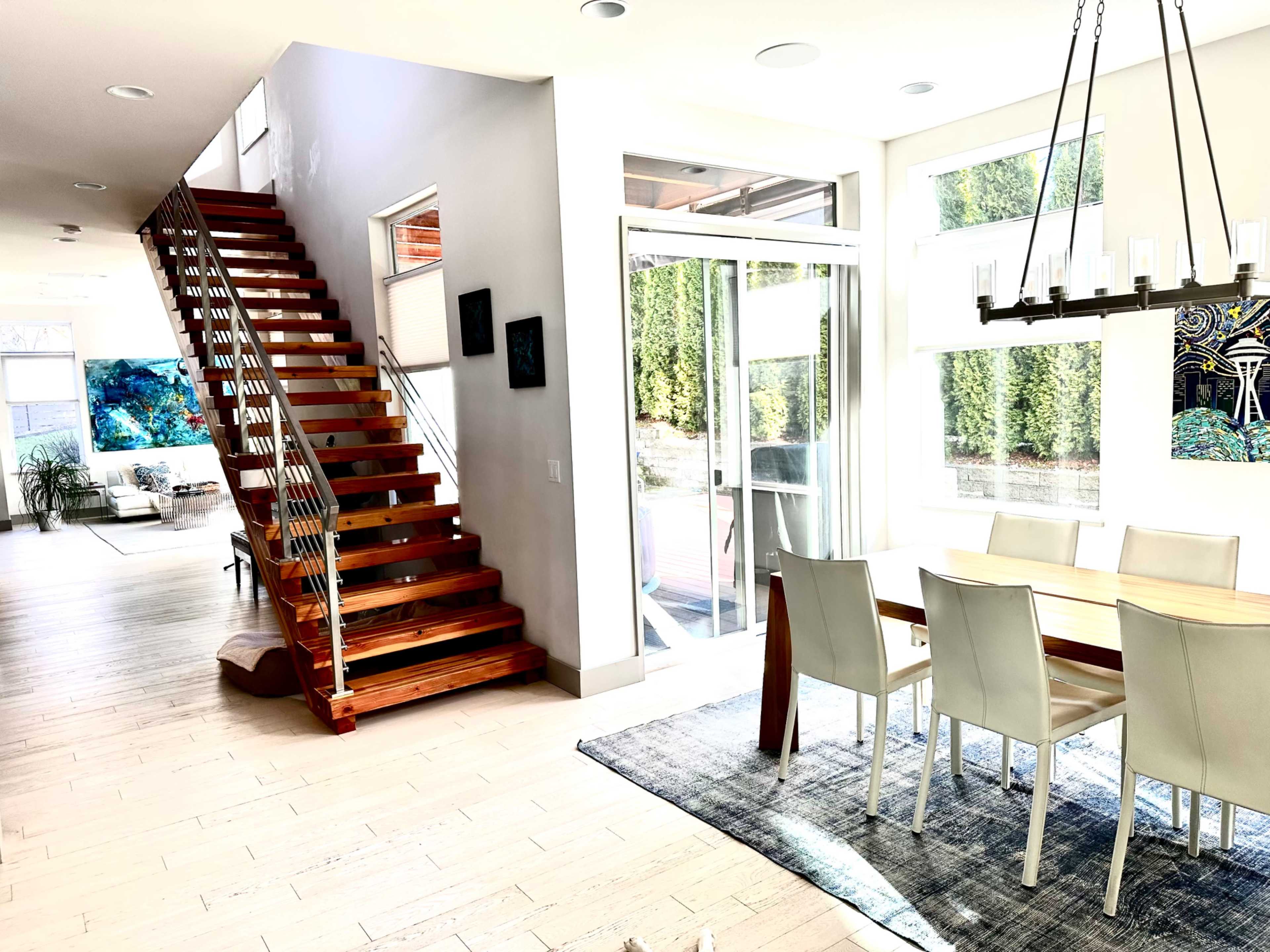 A modern interior features a wooden staircase leading to an upper level, with a dining area and large windows offering natural light.