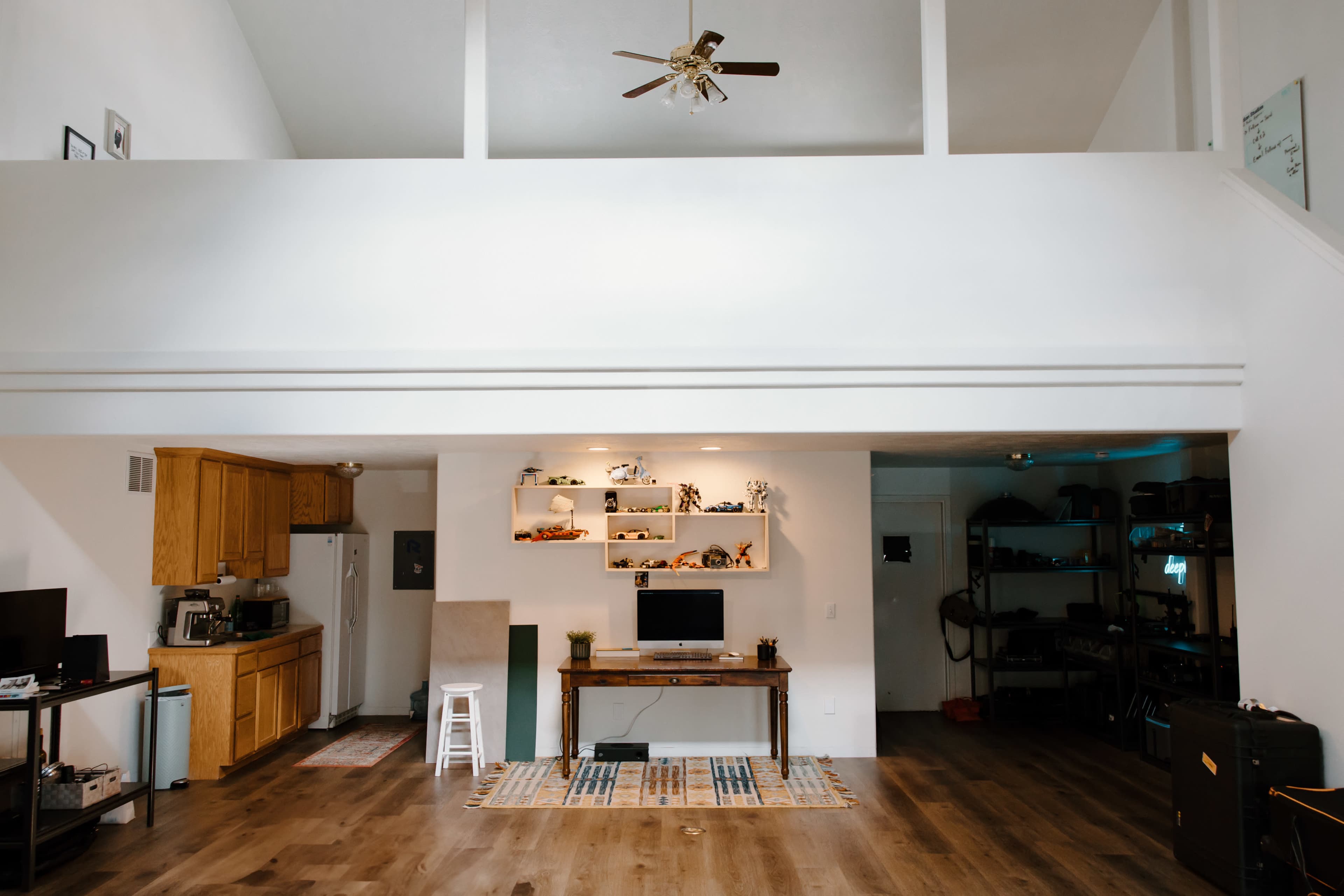 A spacious, open-concept living area with a kitchen, a work desk, and shelves displaying various objects.