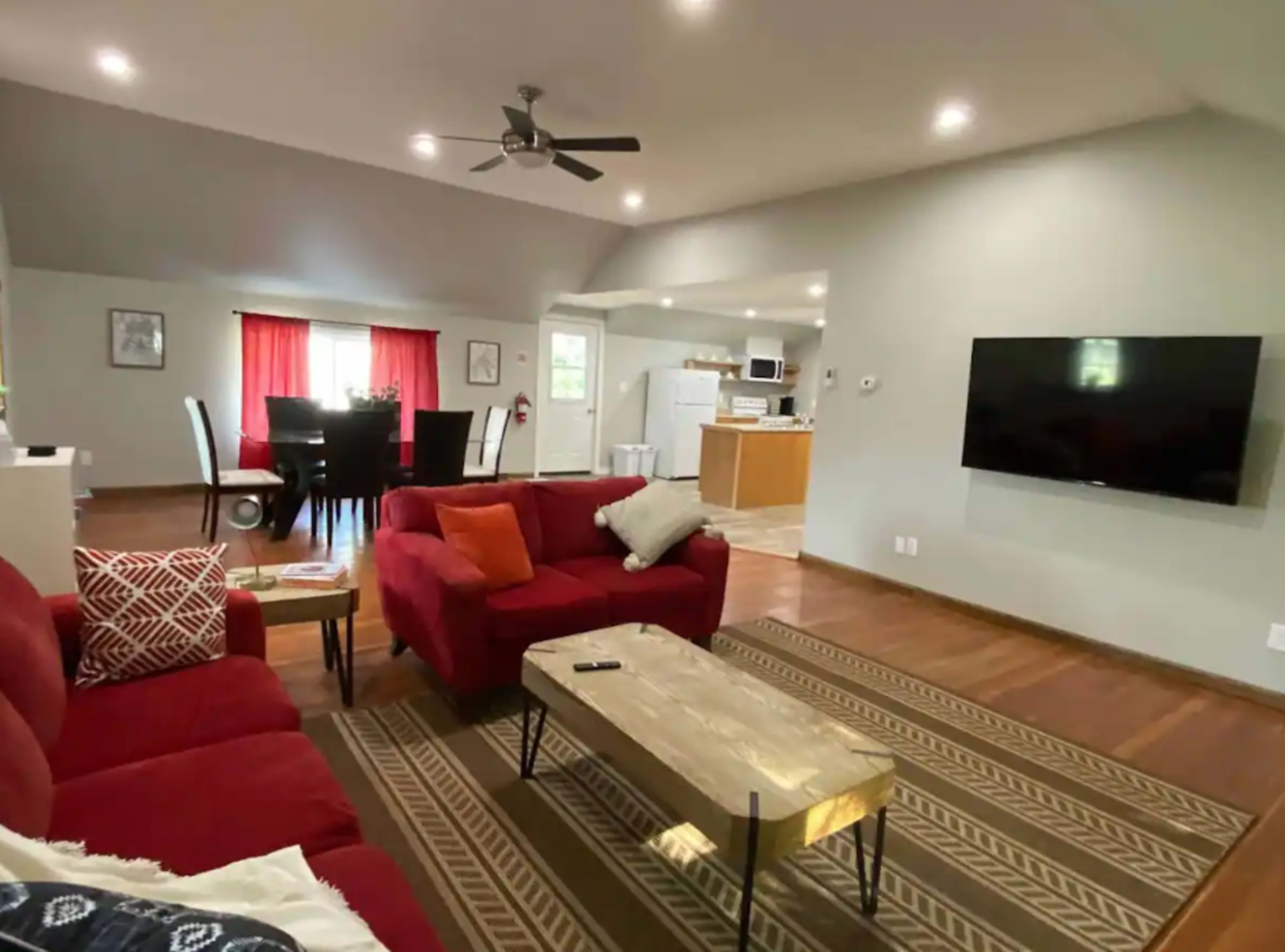 The living room features red sofas, a coffee table, and a television mounted on a gray wall, with a dining area visible in the background.