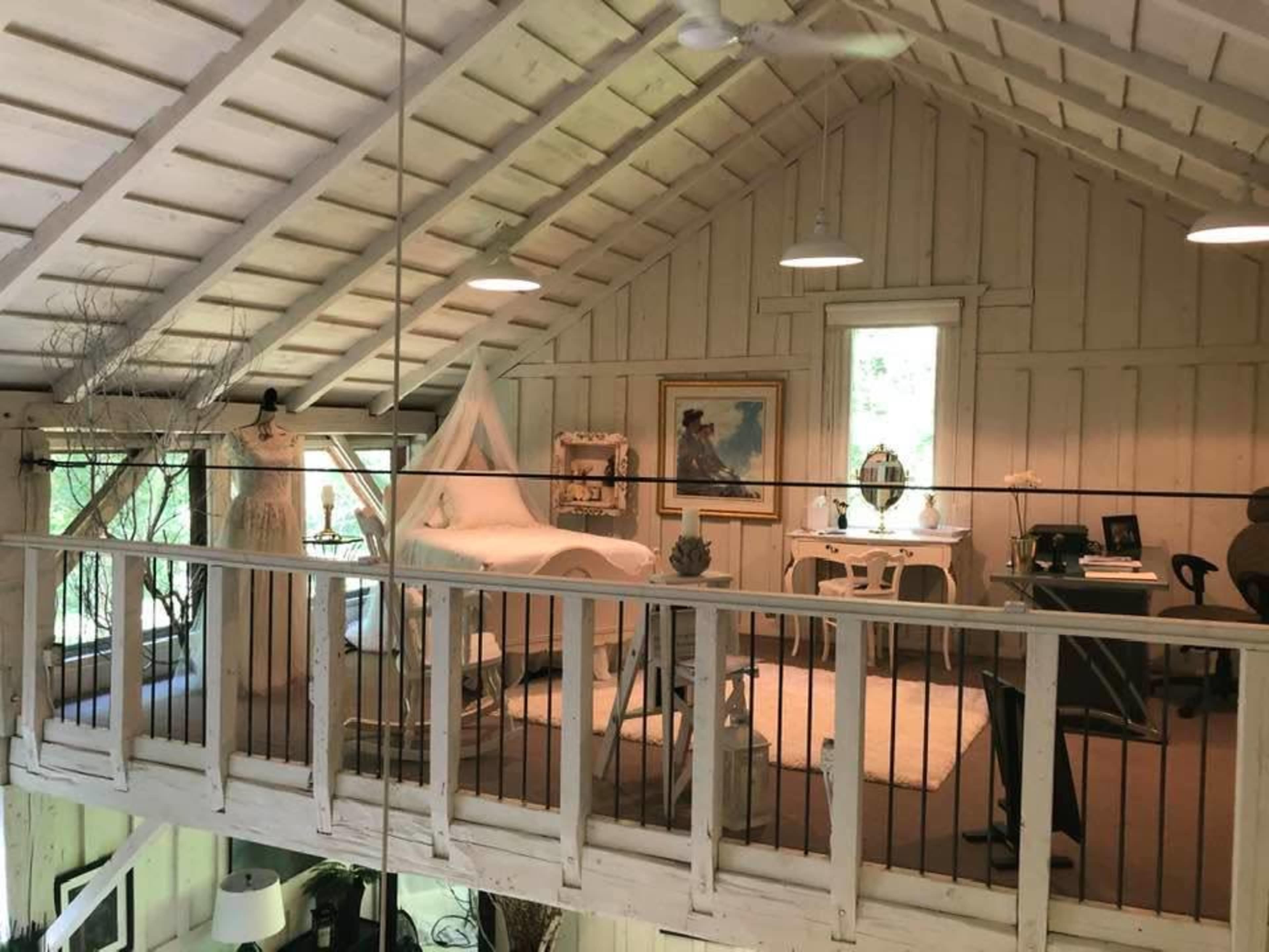 A well-lit loft space with a wooden ceiling, featuring a bed, a desk, and various decor items.