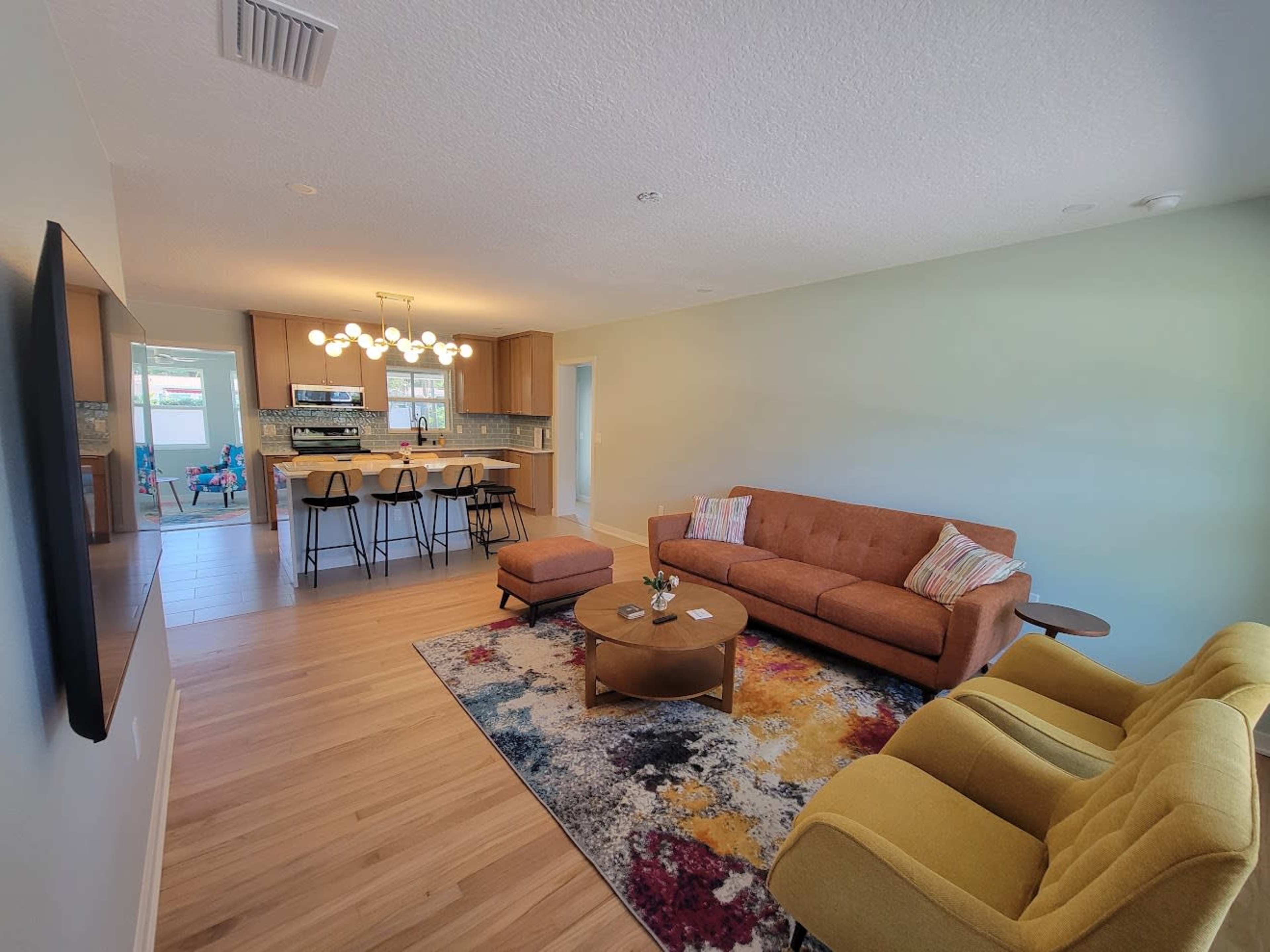 The image shows a modern, open-concept living area with a couch, two armchairs, a coffee table, and a kitchen visible in the background.